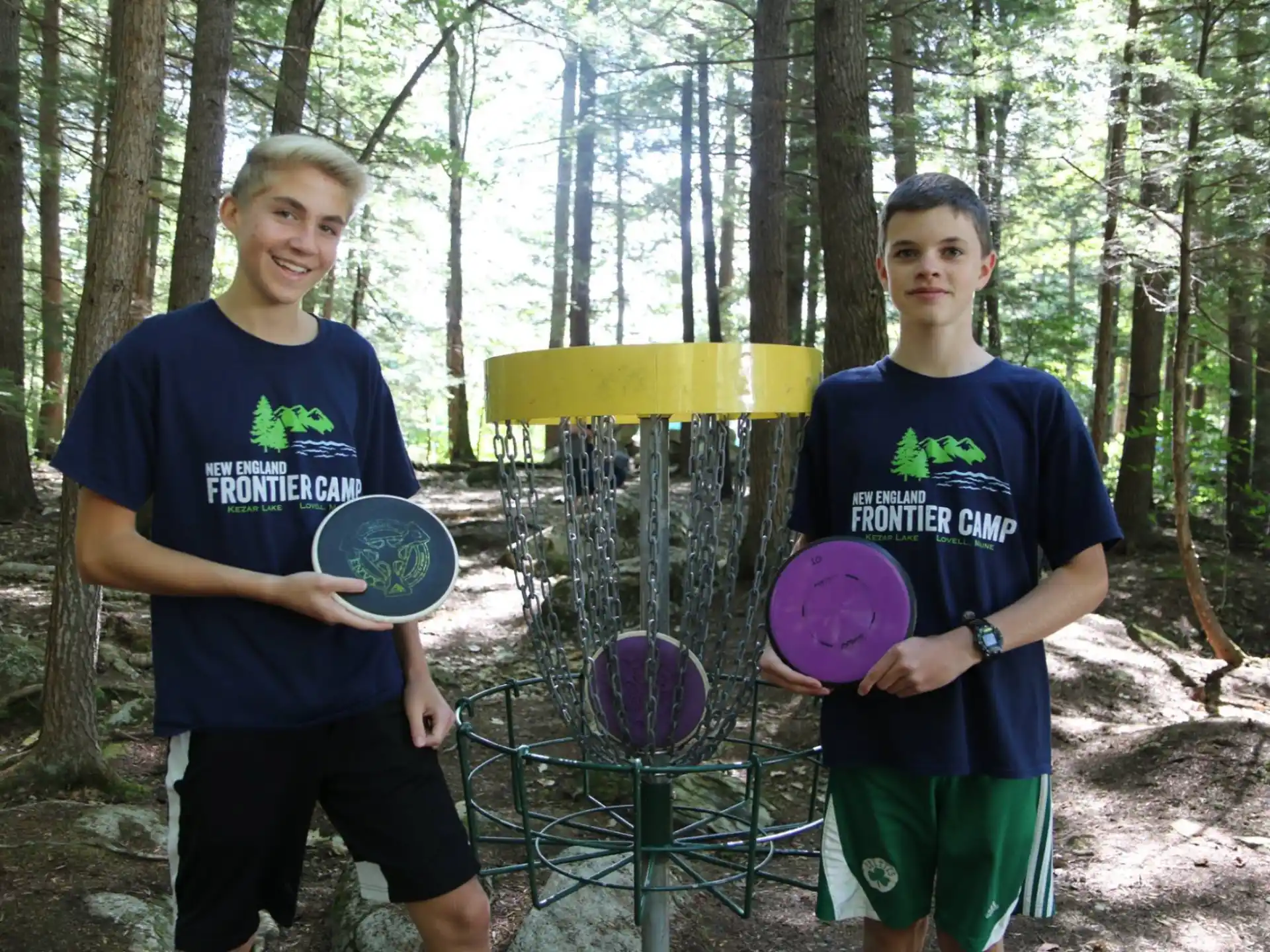 a couple of boys holding frisbees in a park