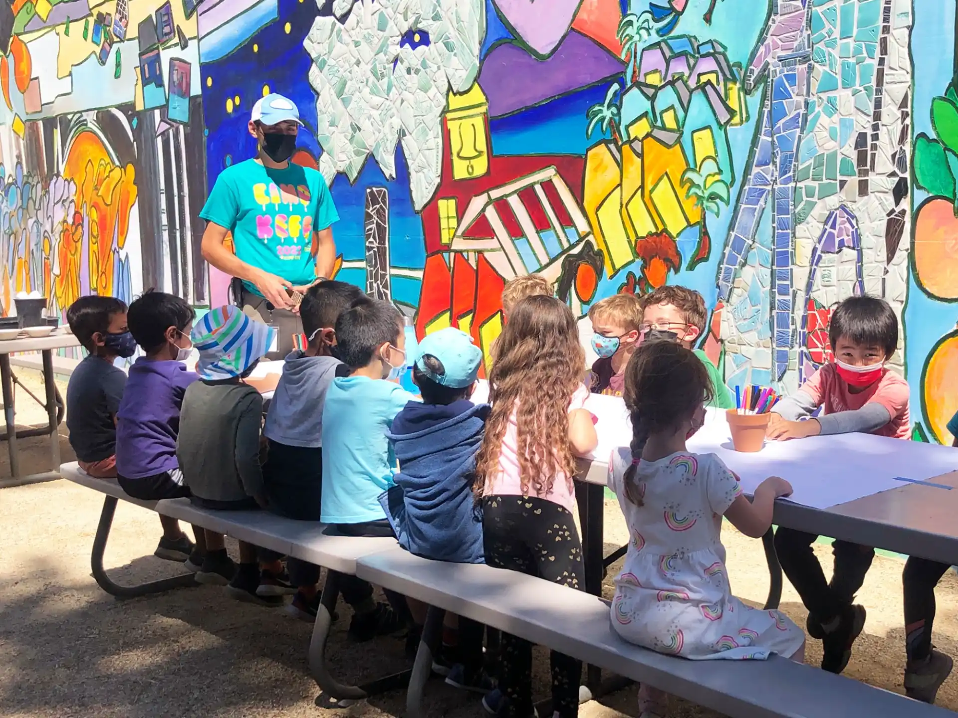 a group of children sitting at a table in front of a wall with graffiti