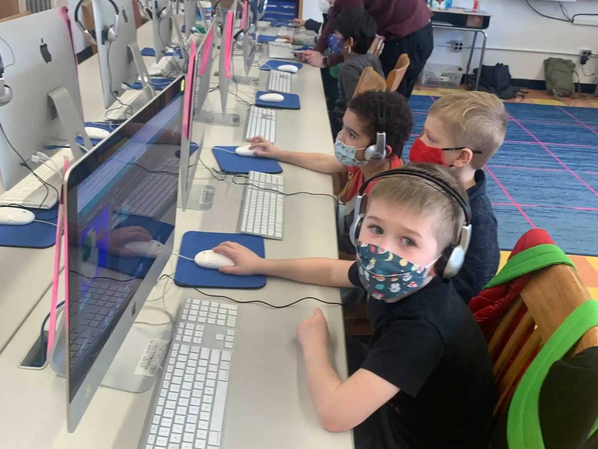 a group of kids sitting at a table with computers