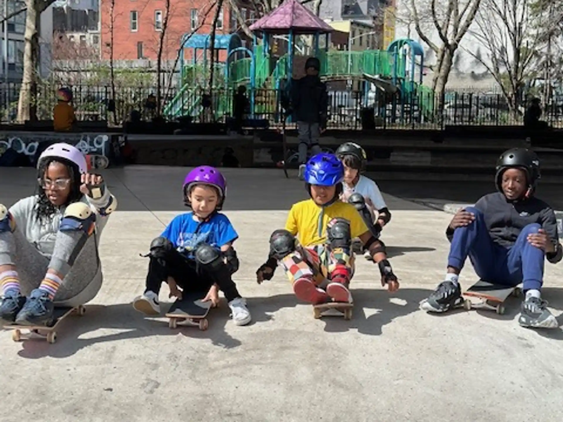 a group of kids sitting on the ground wearing helmets