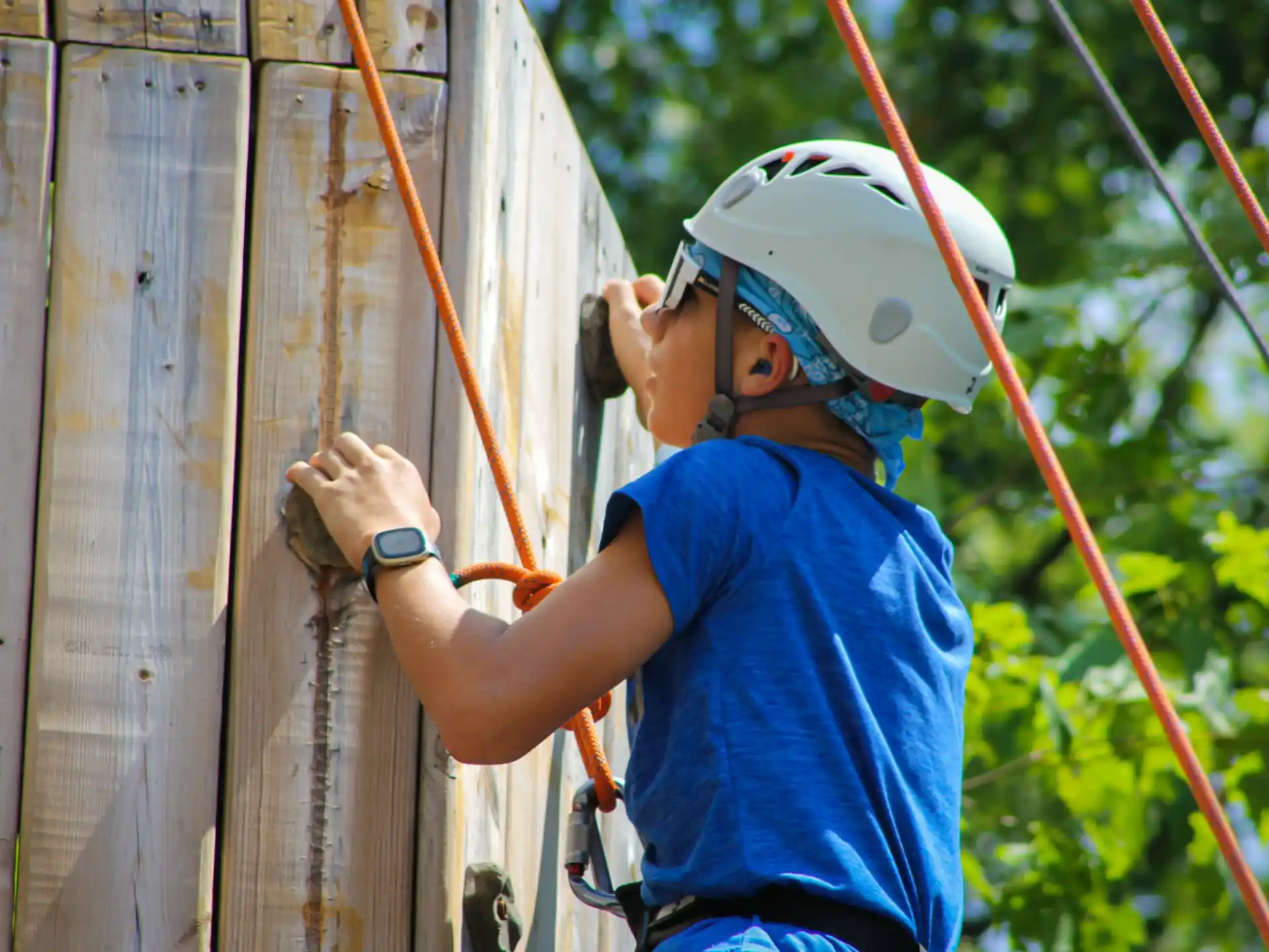 a young boy wearing a helmet and holding a rope to a wooden fence