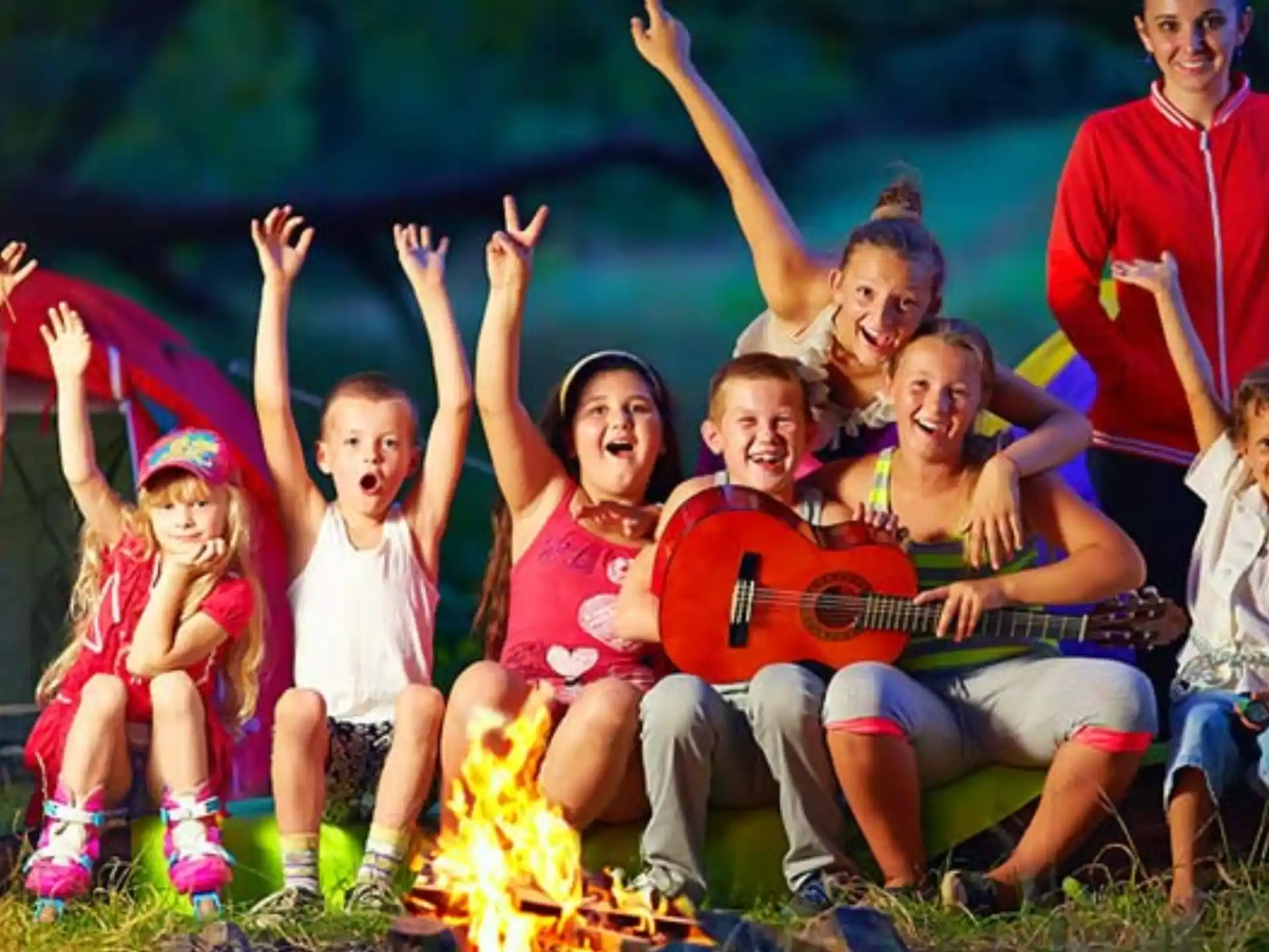 a group of kids sitting on the grass with a person playing guitar