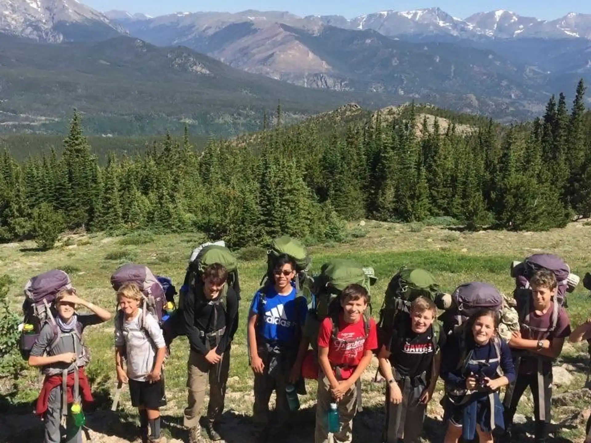 a group of people wearing helmets and standing on a grassy hill with trees and mountains in the background