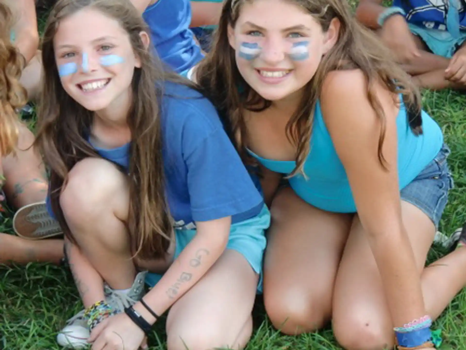 a couple of girls with painted faces sitting on grass
