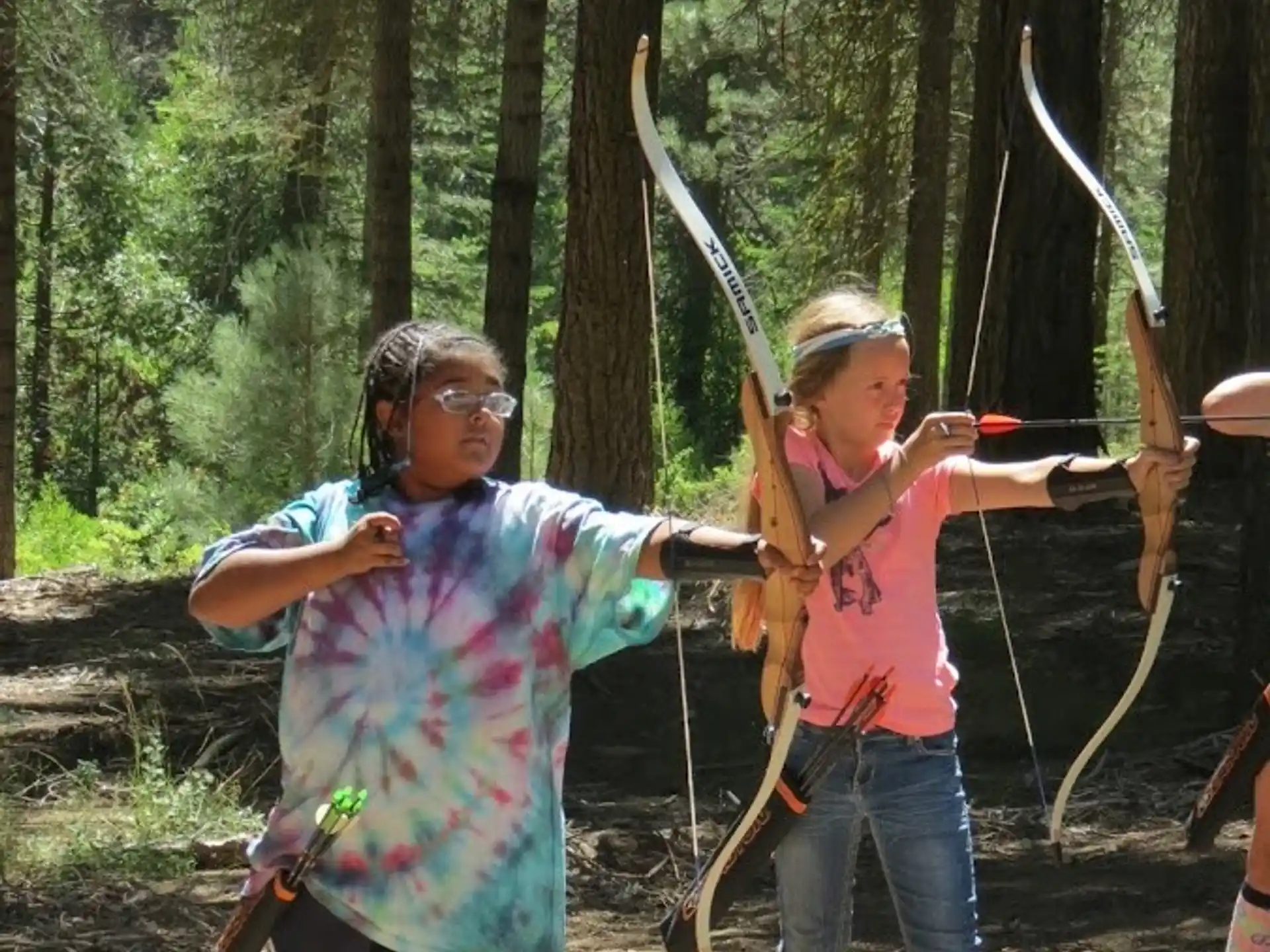 a person and a girl holding bows and arrows in the woods
