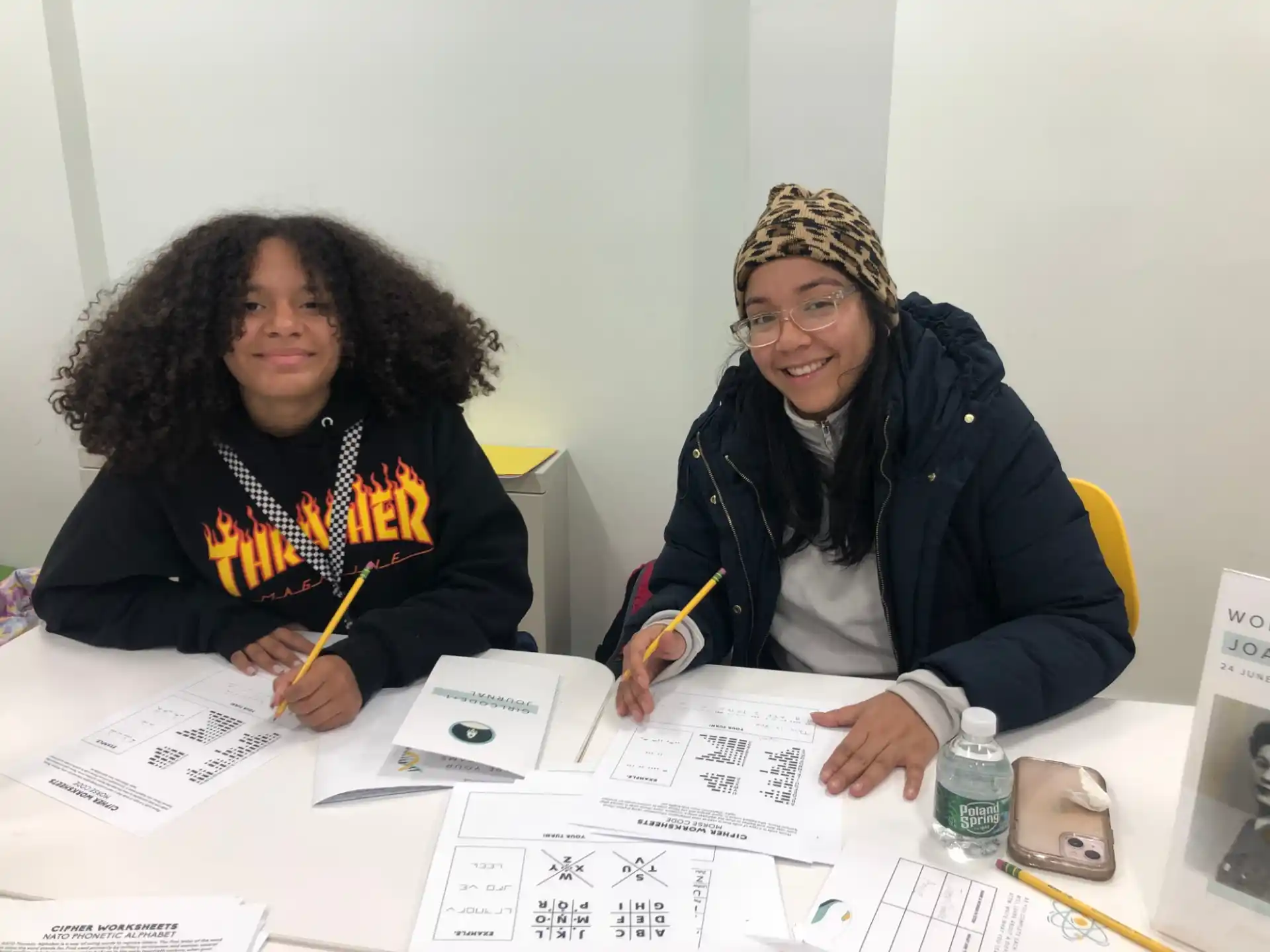 a couple of women sitting at a table with papers and pens