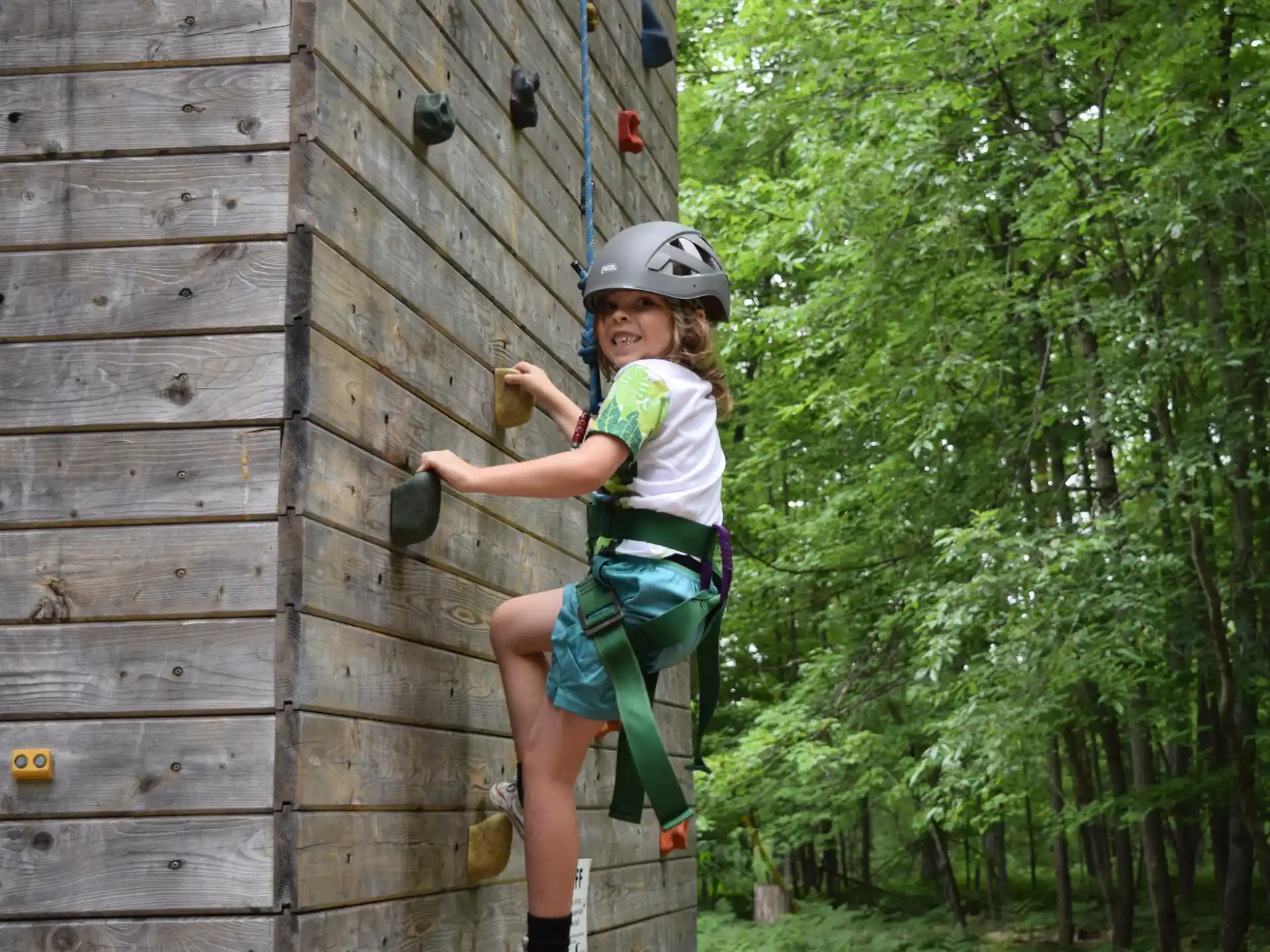a girl wearing a helmet and climbing a wooden fence