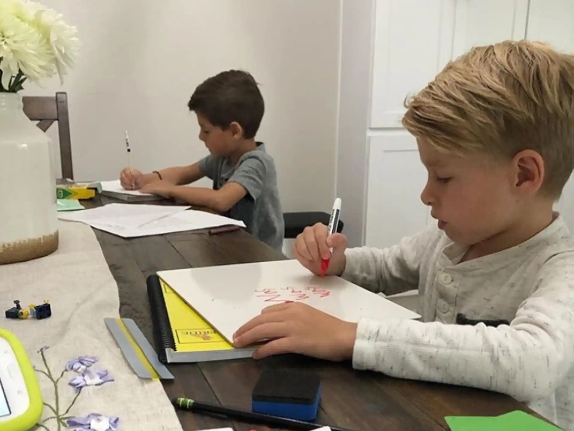 a few young boys sitting at a table writing on paper