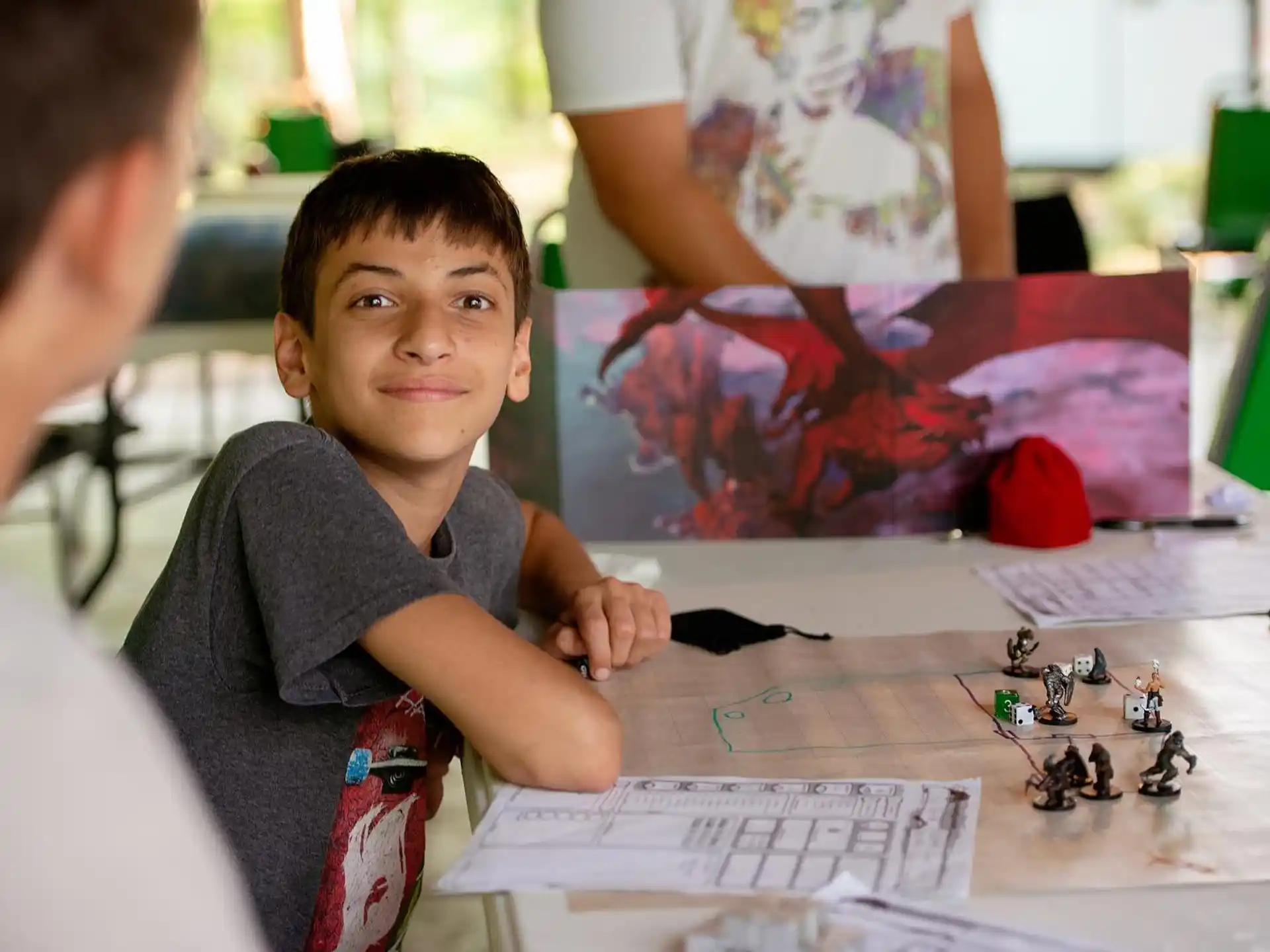 a boy sitting at a table with a board game and a person standing behind him