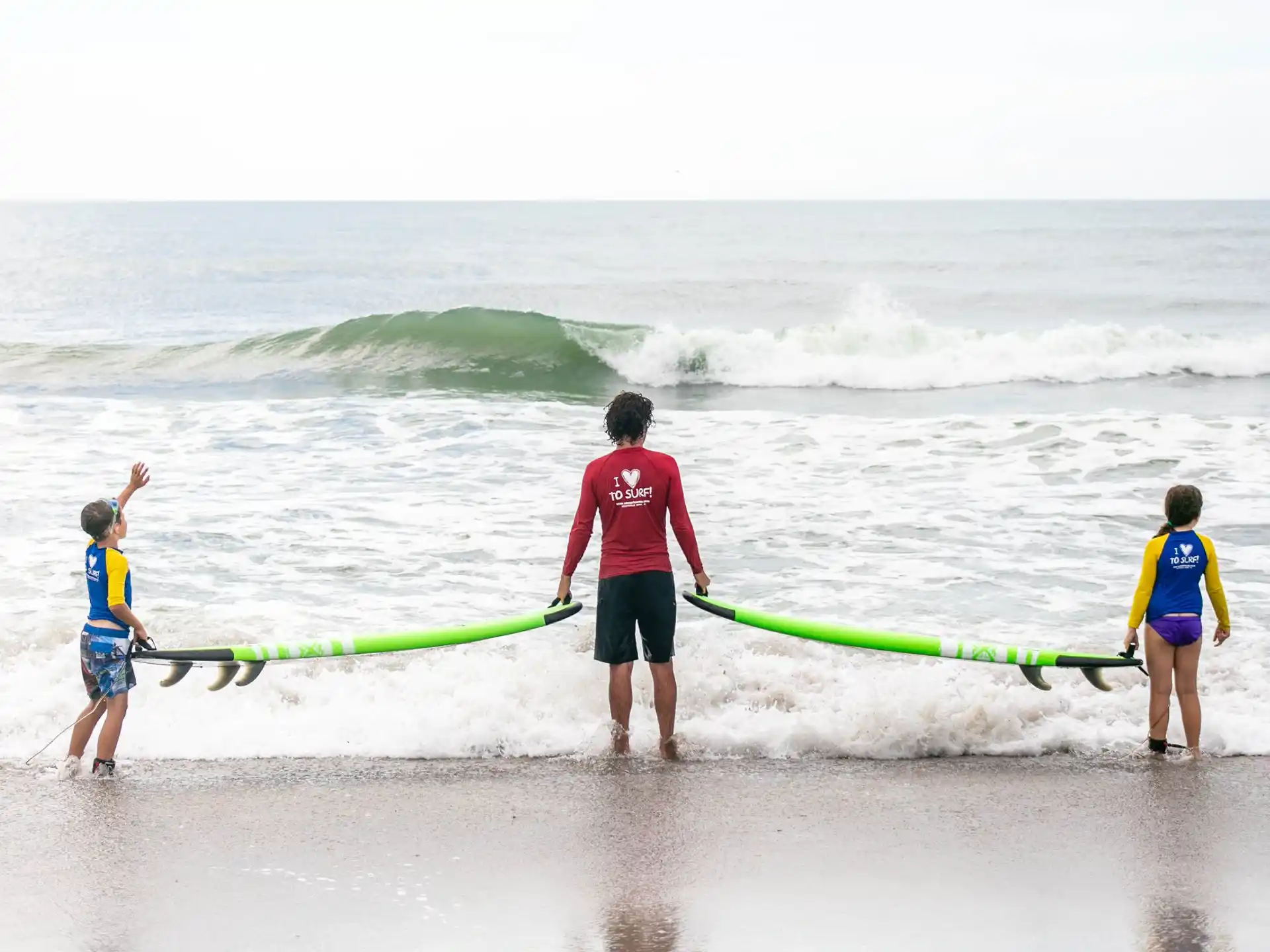 a man and a couple of kids stand on the beach with surfboards