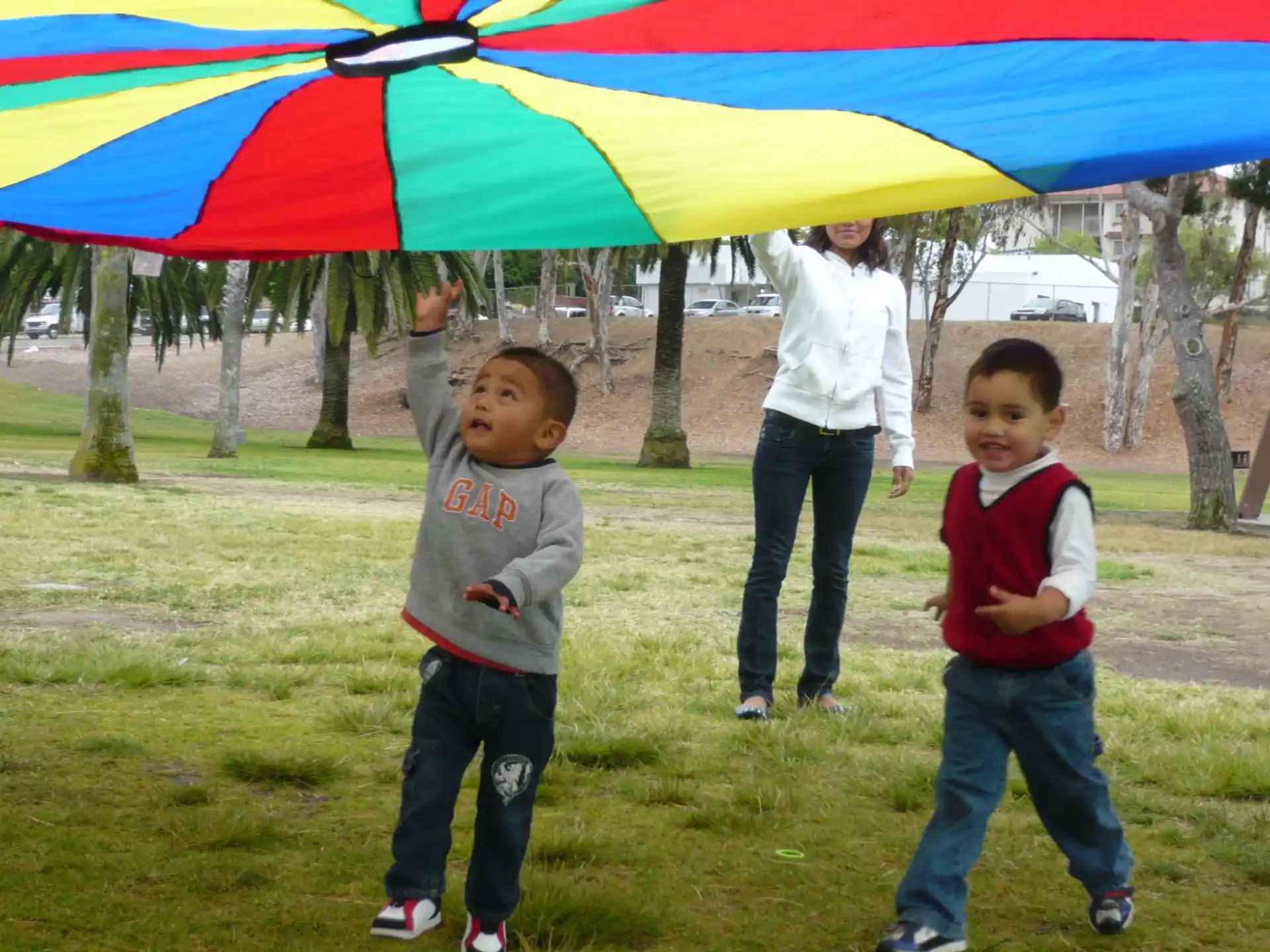 a couple of kids stand under a colorful umbrella