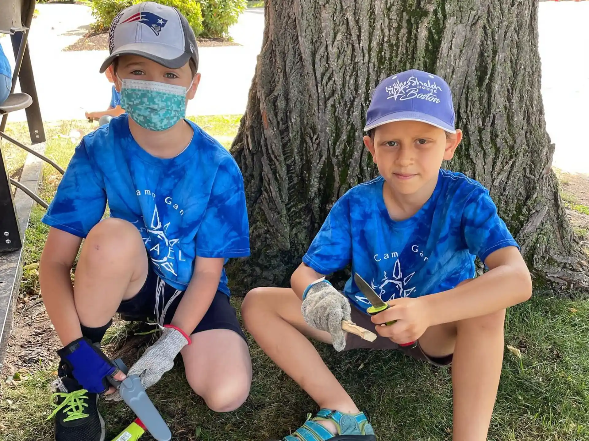 two boys wearing masks and sitting next to a tree