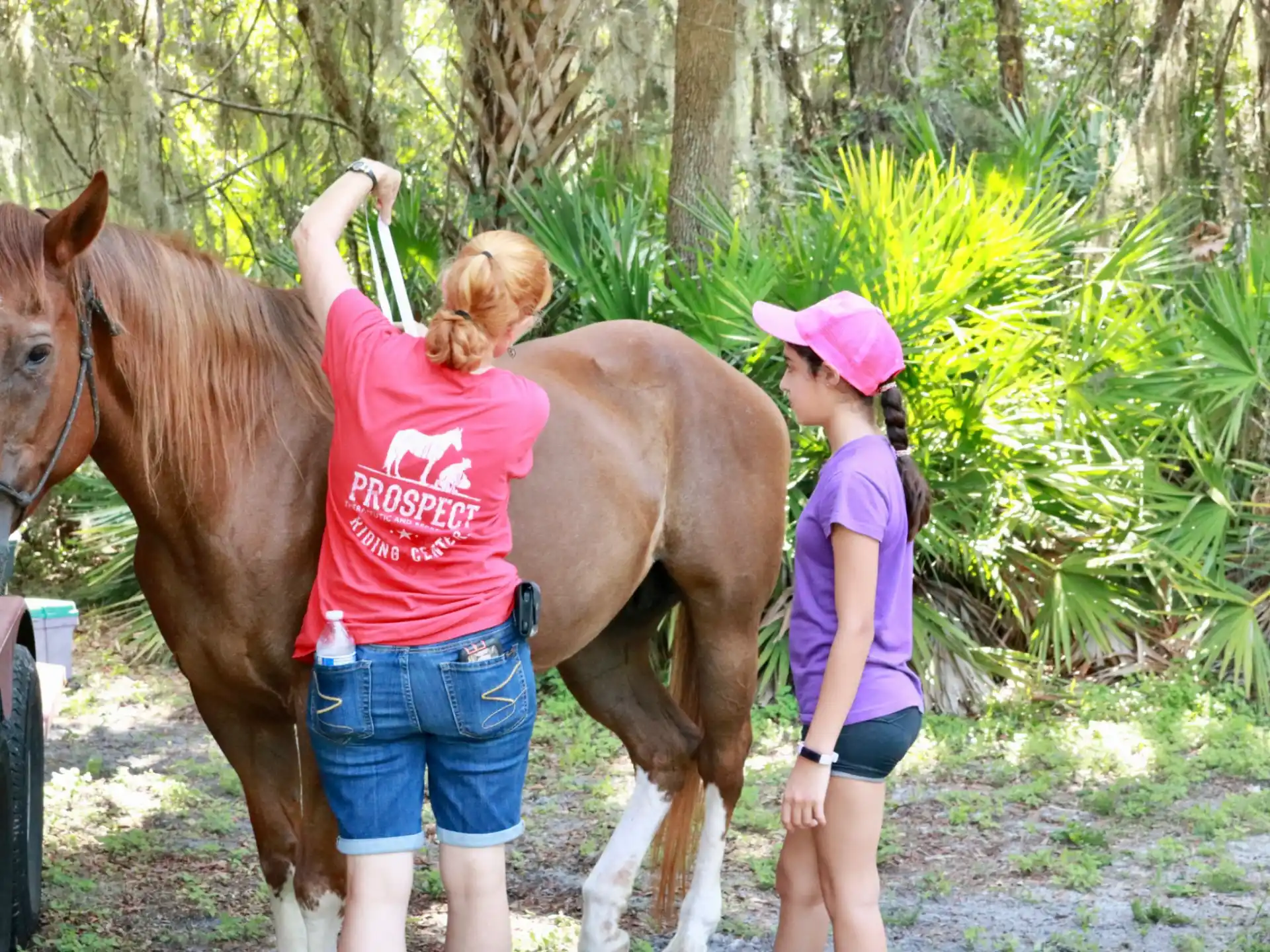 a couple of girls stand near a horse