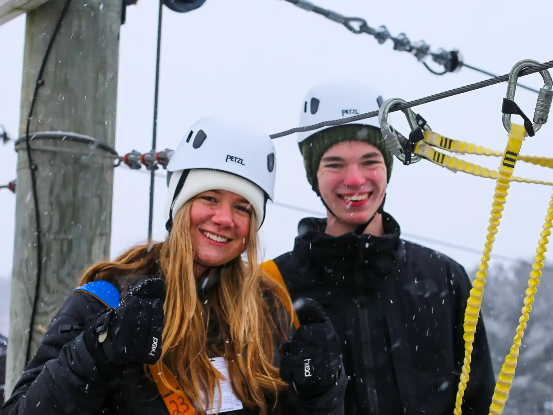a couple of people wearing helmets and harnesses on a cable