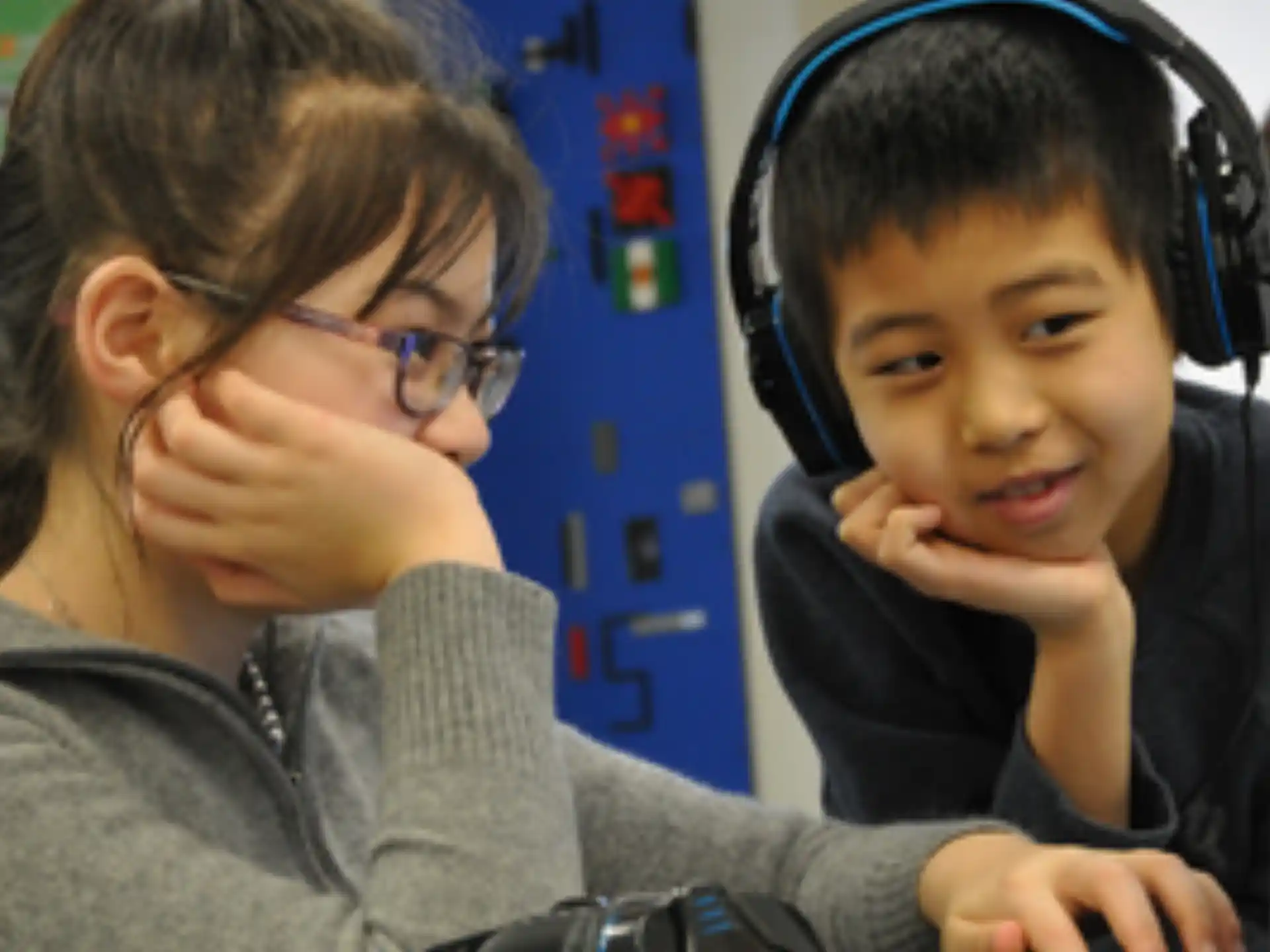 a boy wearing headphones and sitting next to a girl wearing a headset