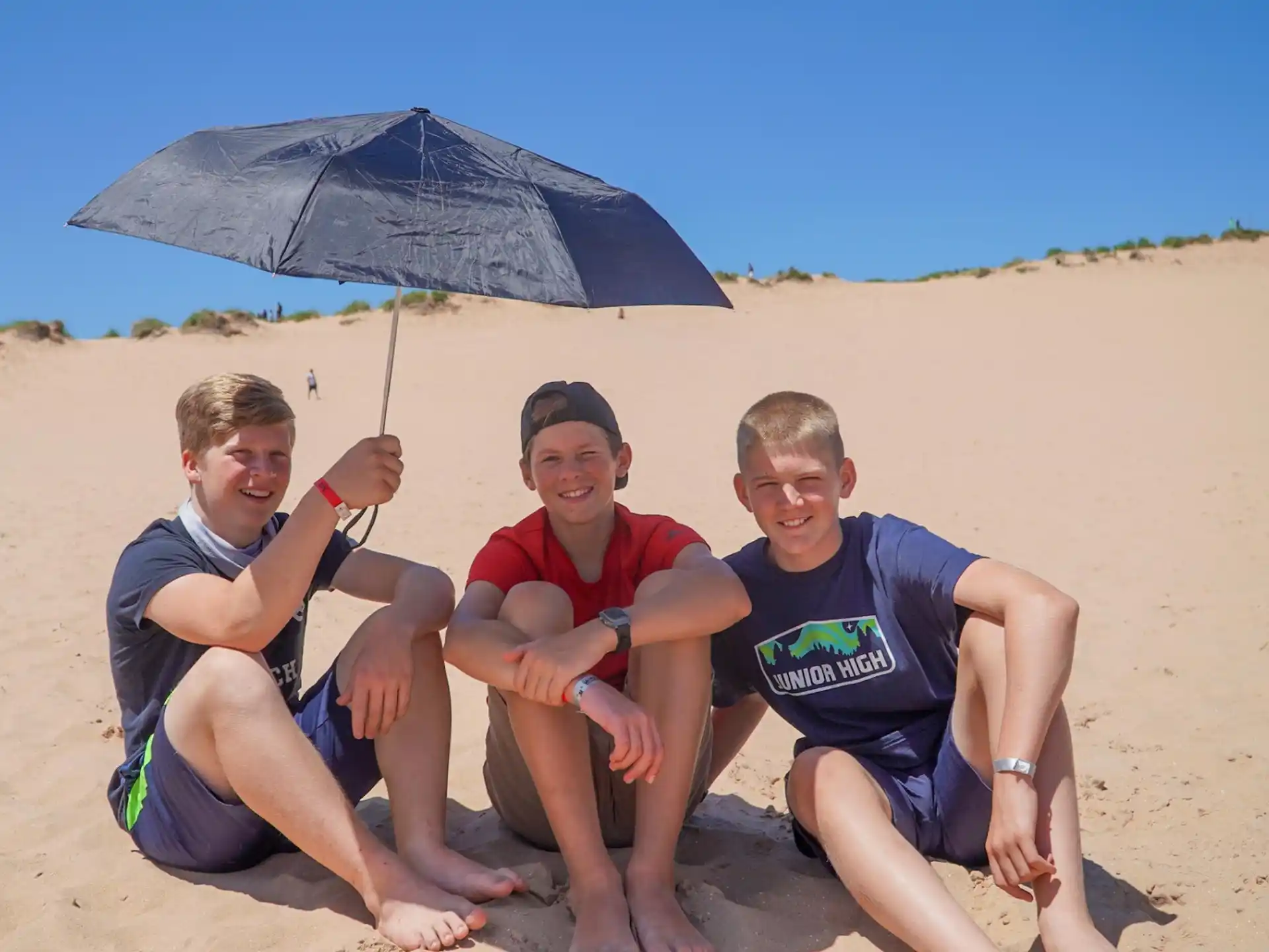 a group of people sitting on a beach under an umbrella
