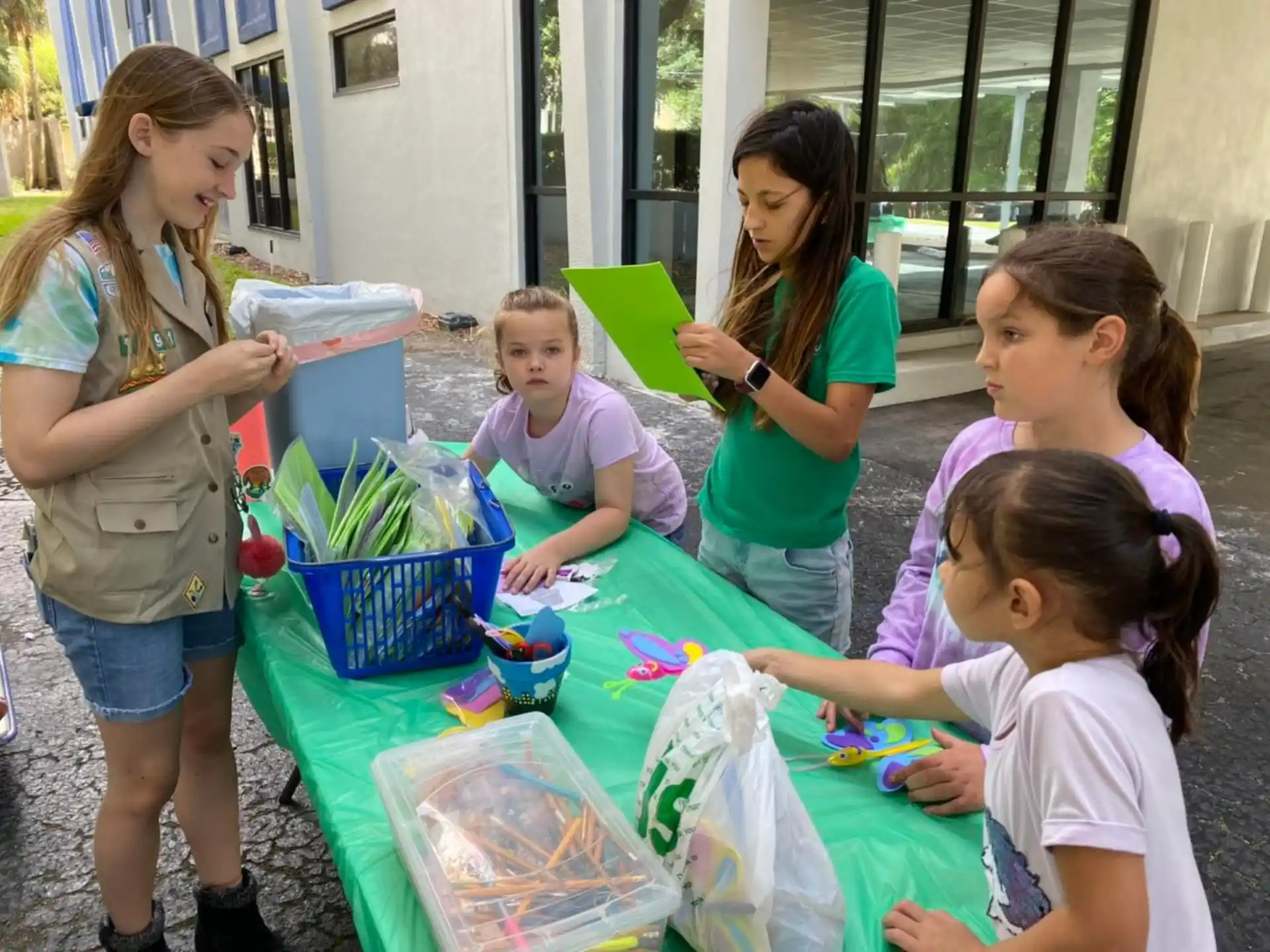 a group of people standing around a table with a green box and a green basket with a green