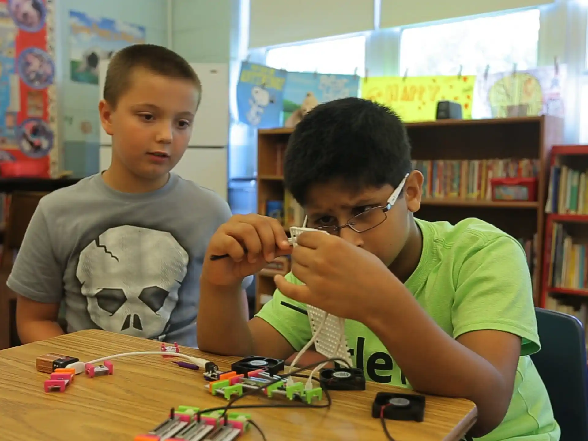 a couple of boys sitting at a table with a game controller