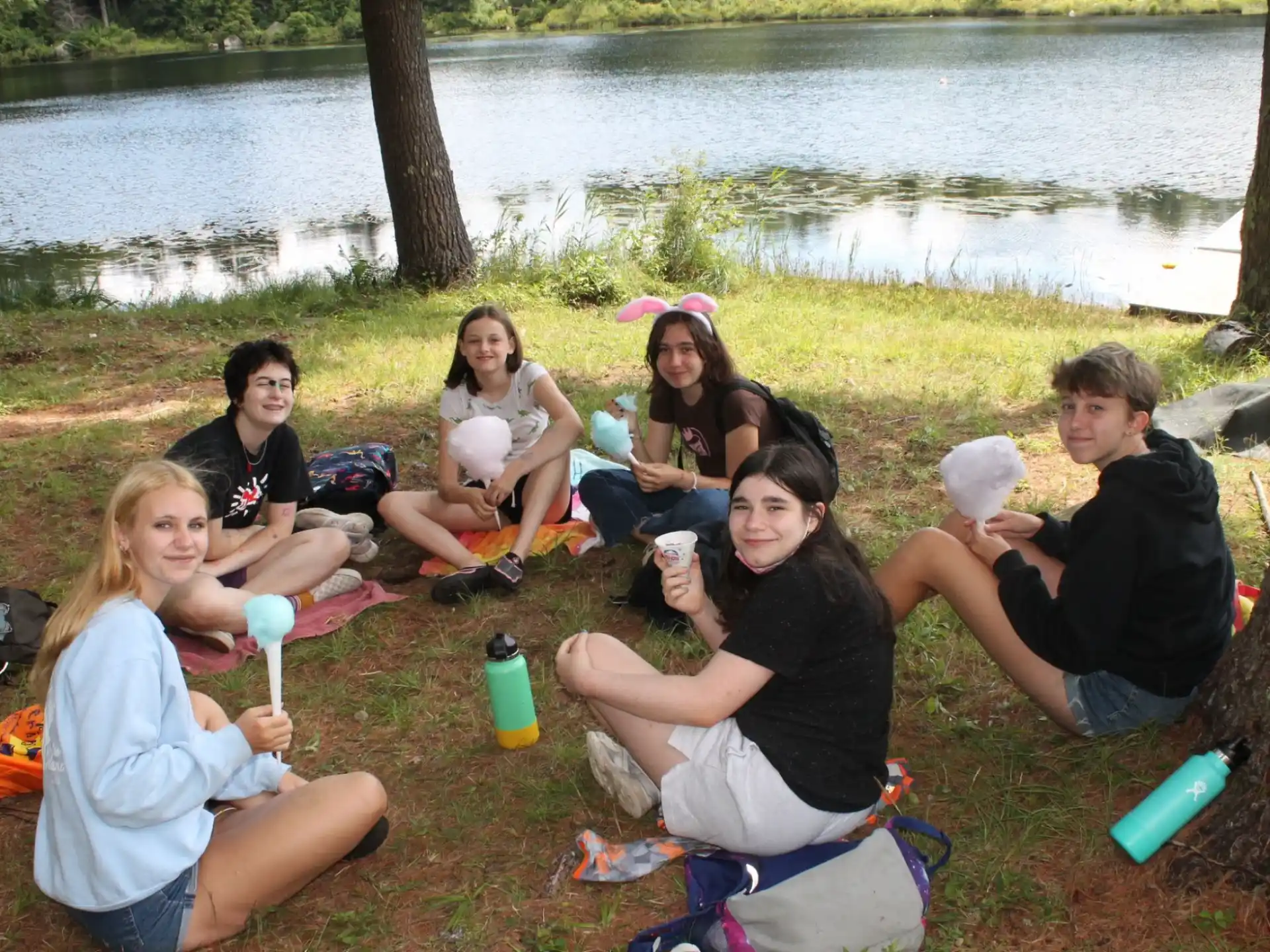 a group of people sitting on the grass by a lake