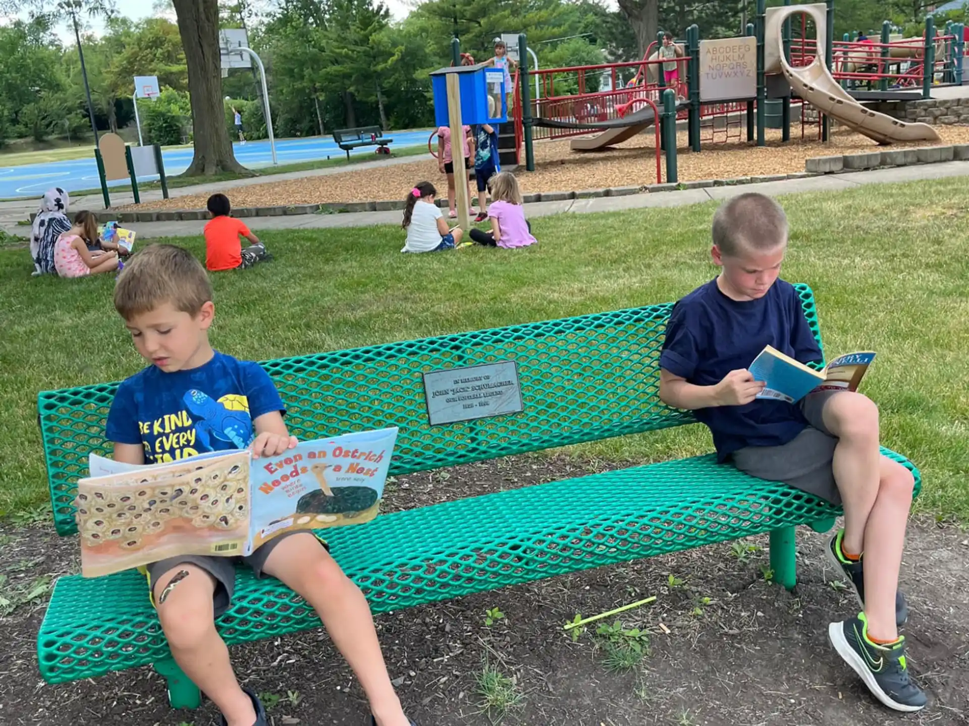 two boys sitting on a bench reading books
