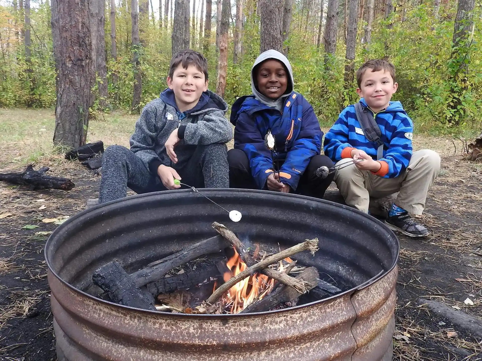 a group of boys sitting next to a fire pit with a campfire