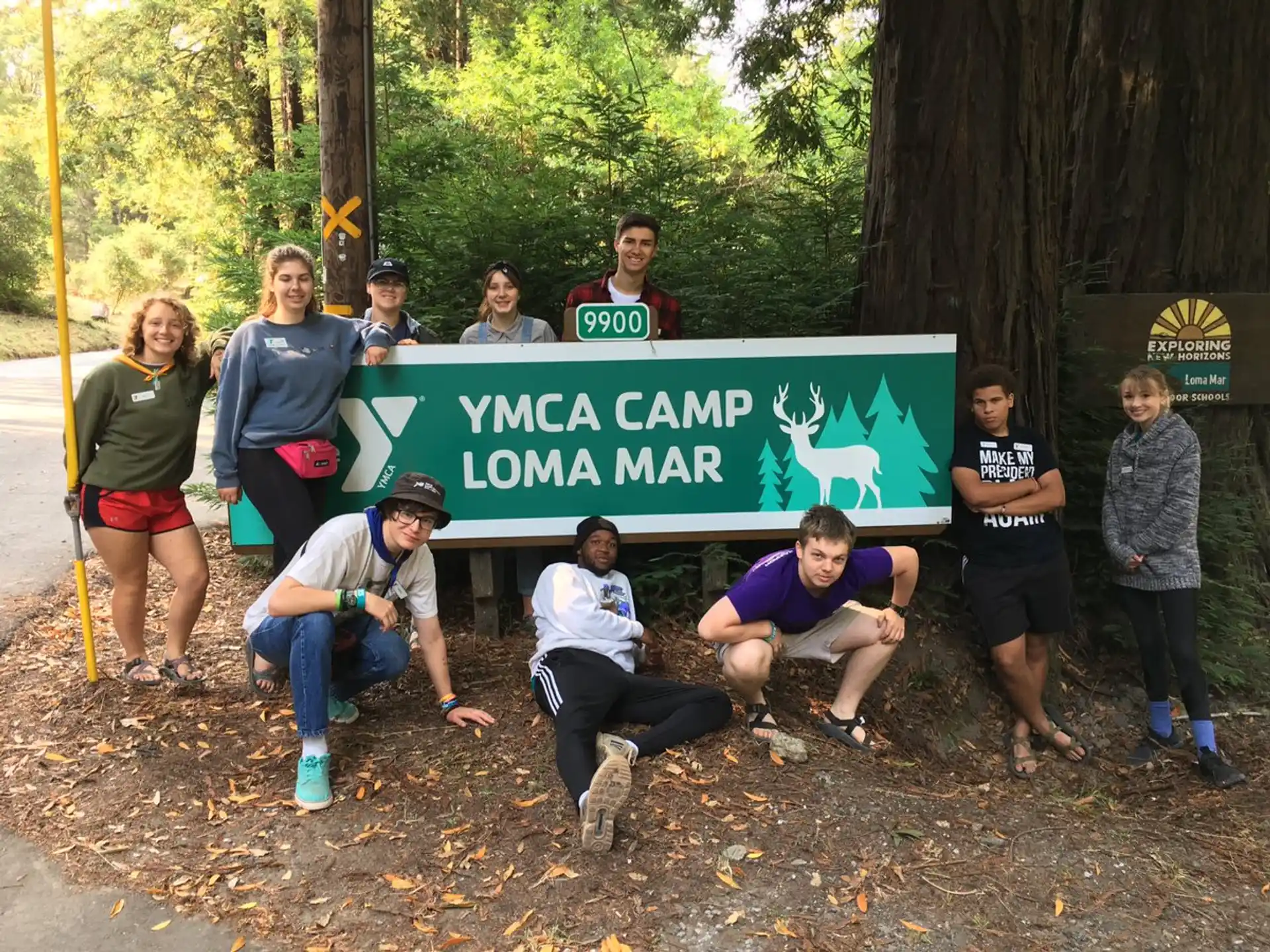 a group of people posing for a photo with a sign in the woods
