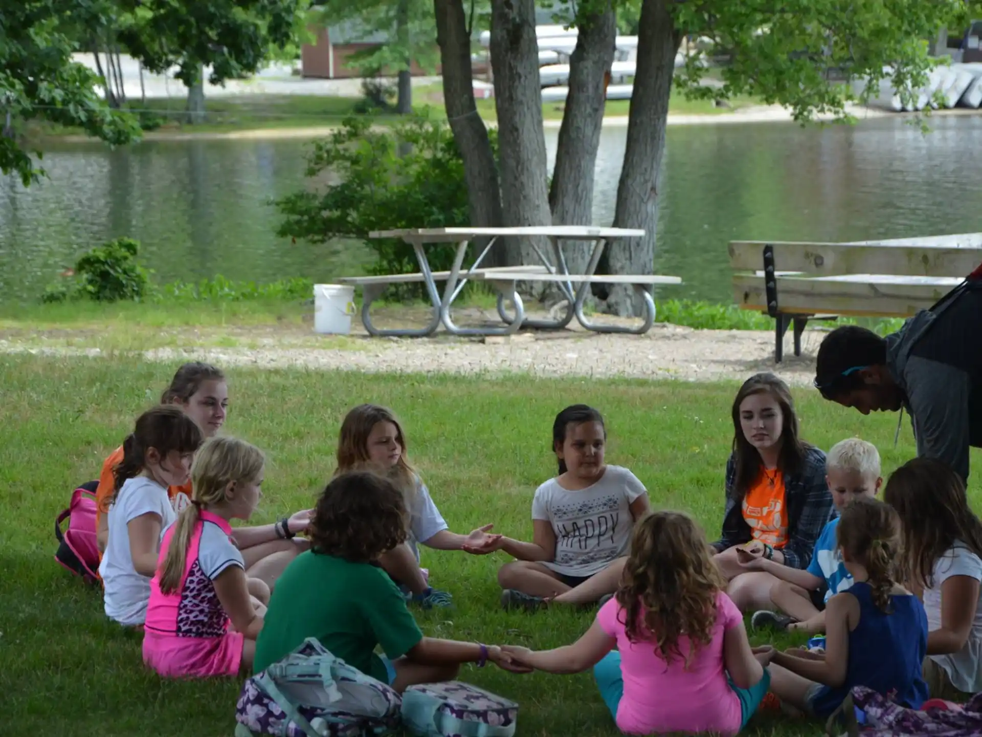 a group of people sitting on the grass by a lake