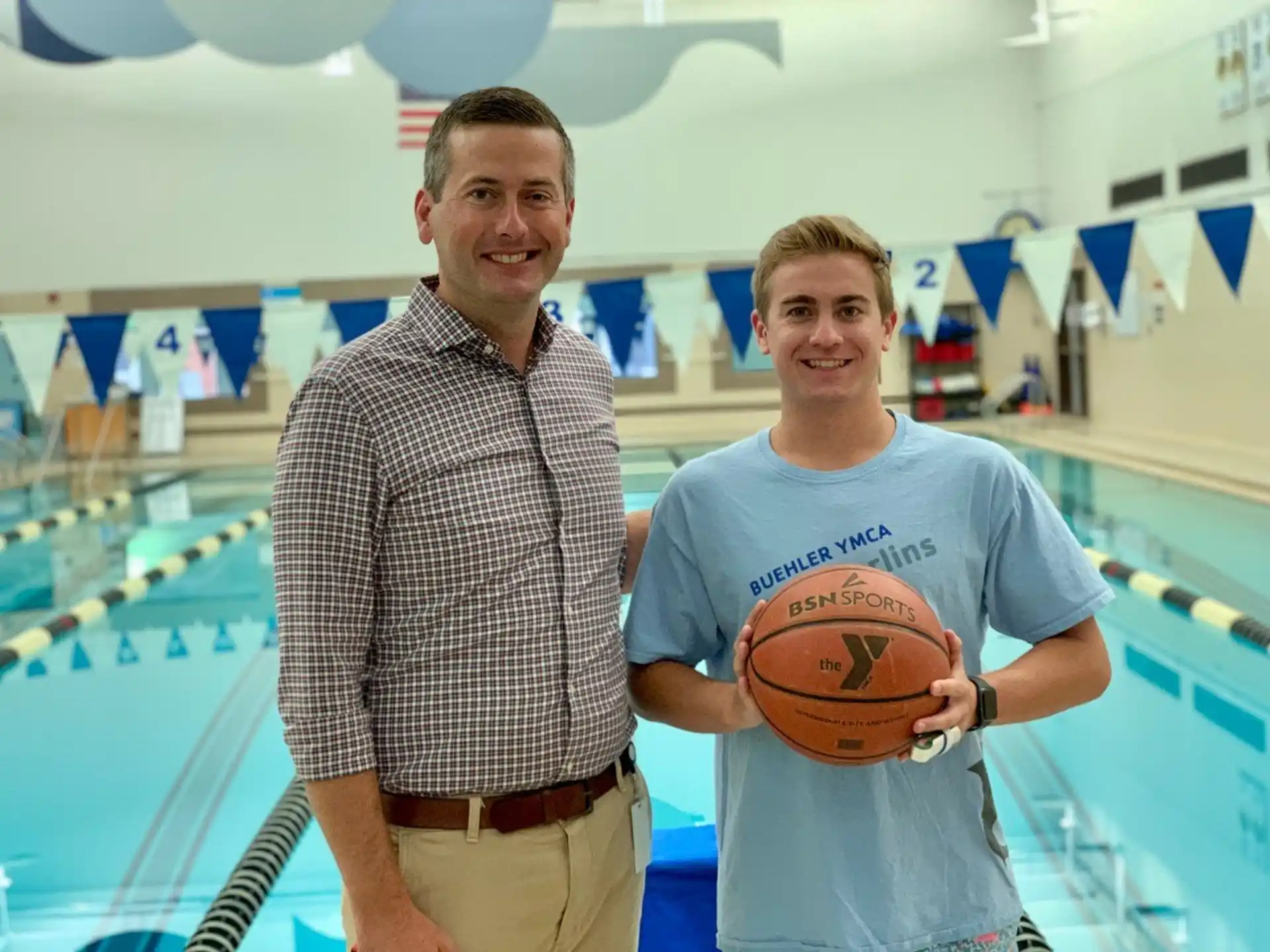 a couple of men posing for a picture next to a swimming pool