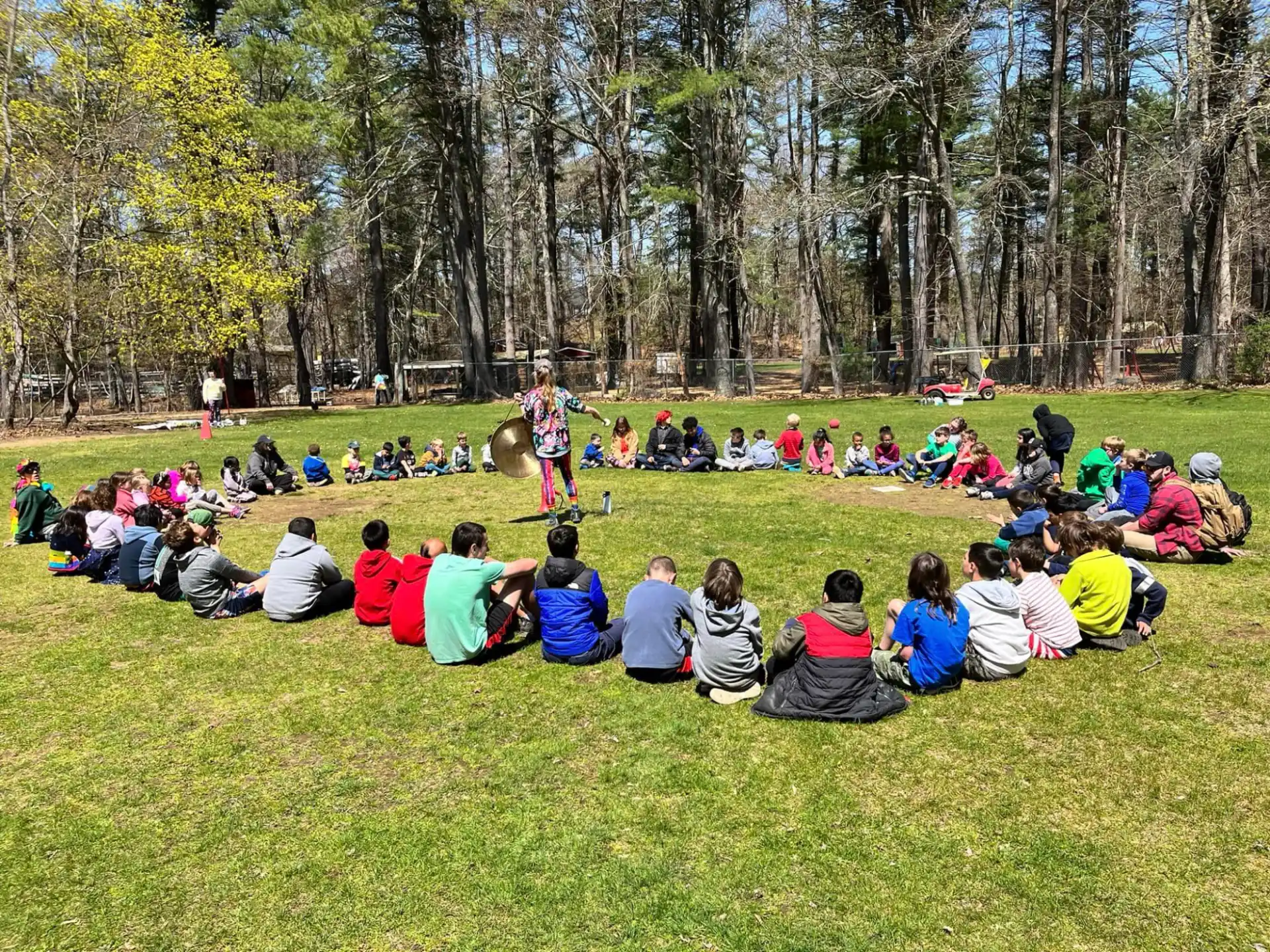 a group of people sitting on the grass watching a person play a guitar