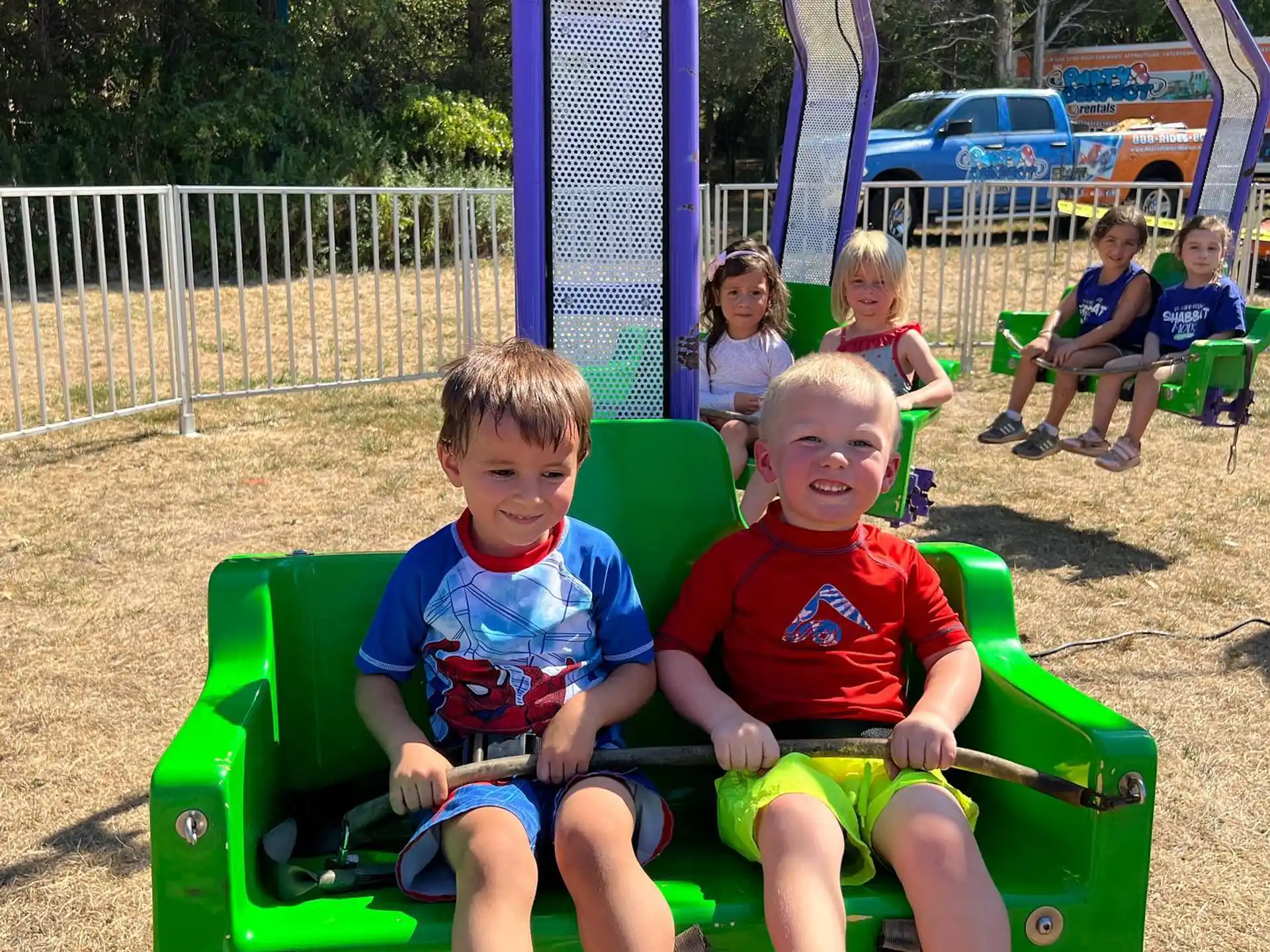 a couple of boys sitting on a green bench in a park