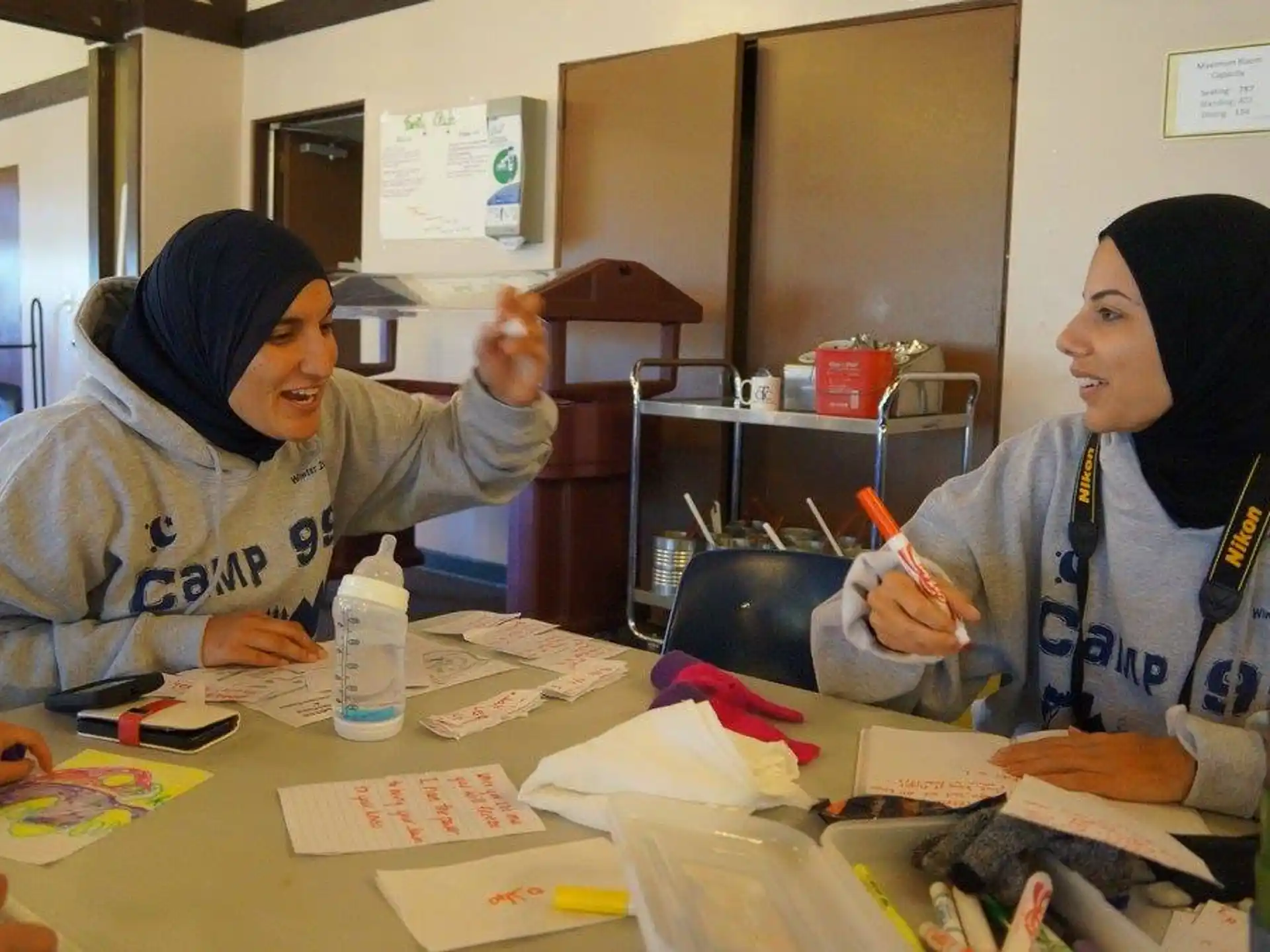 a couple of women sitting at a table with papers and pens