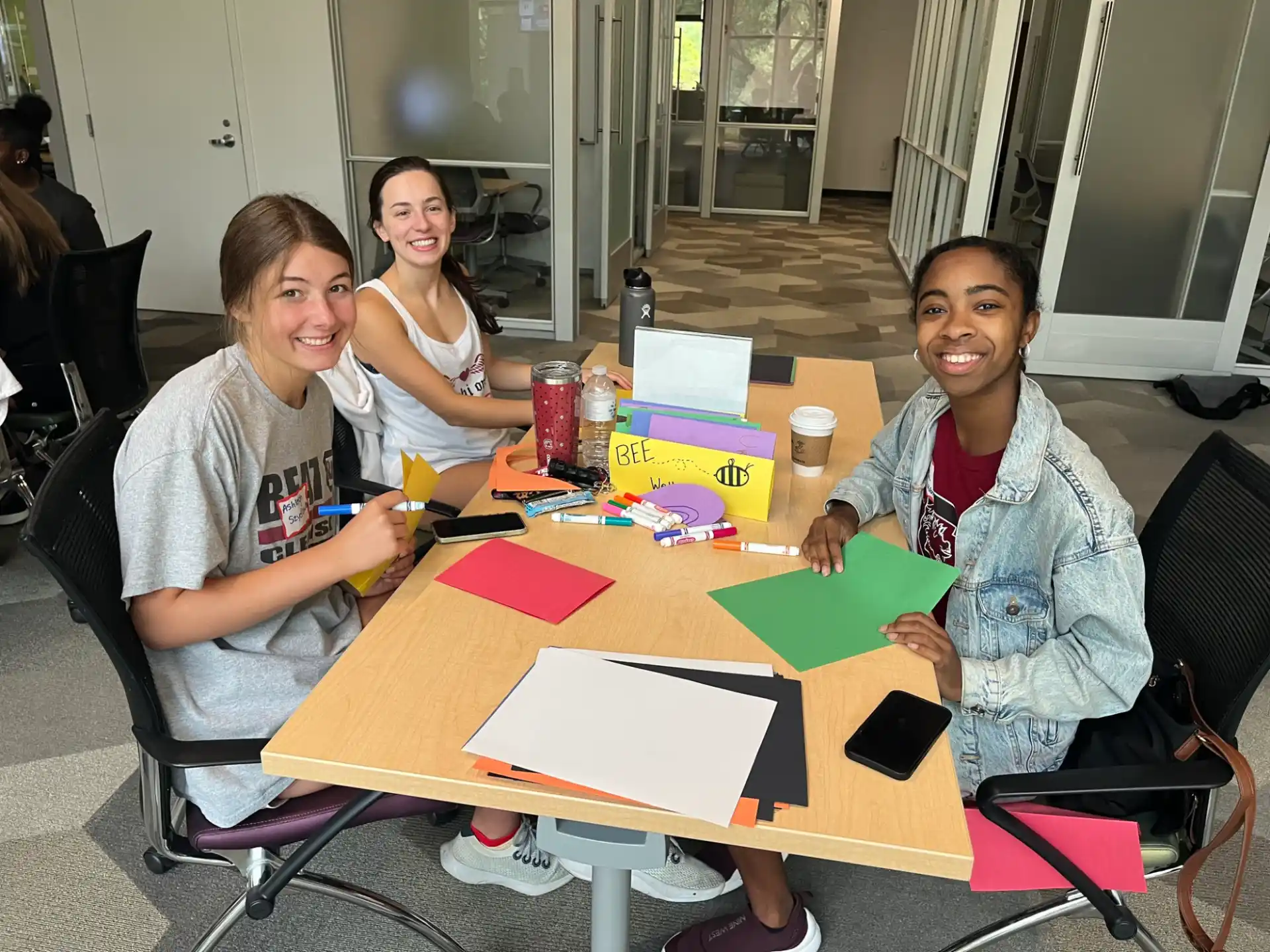 a group of women sitting at a table with colorful paper and pens
