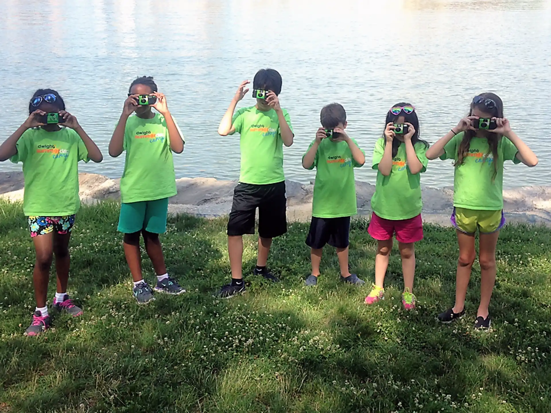 a group of people wearing green shirts and standing on grass by water