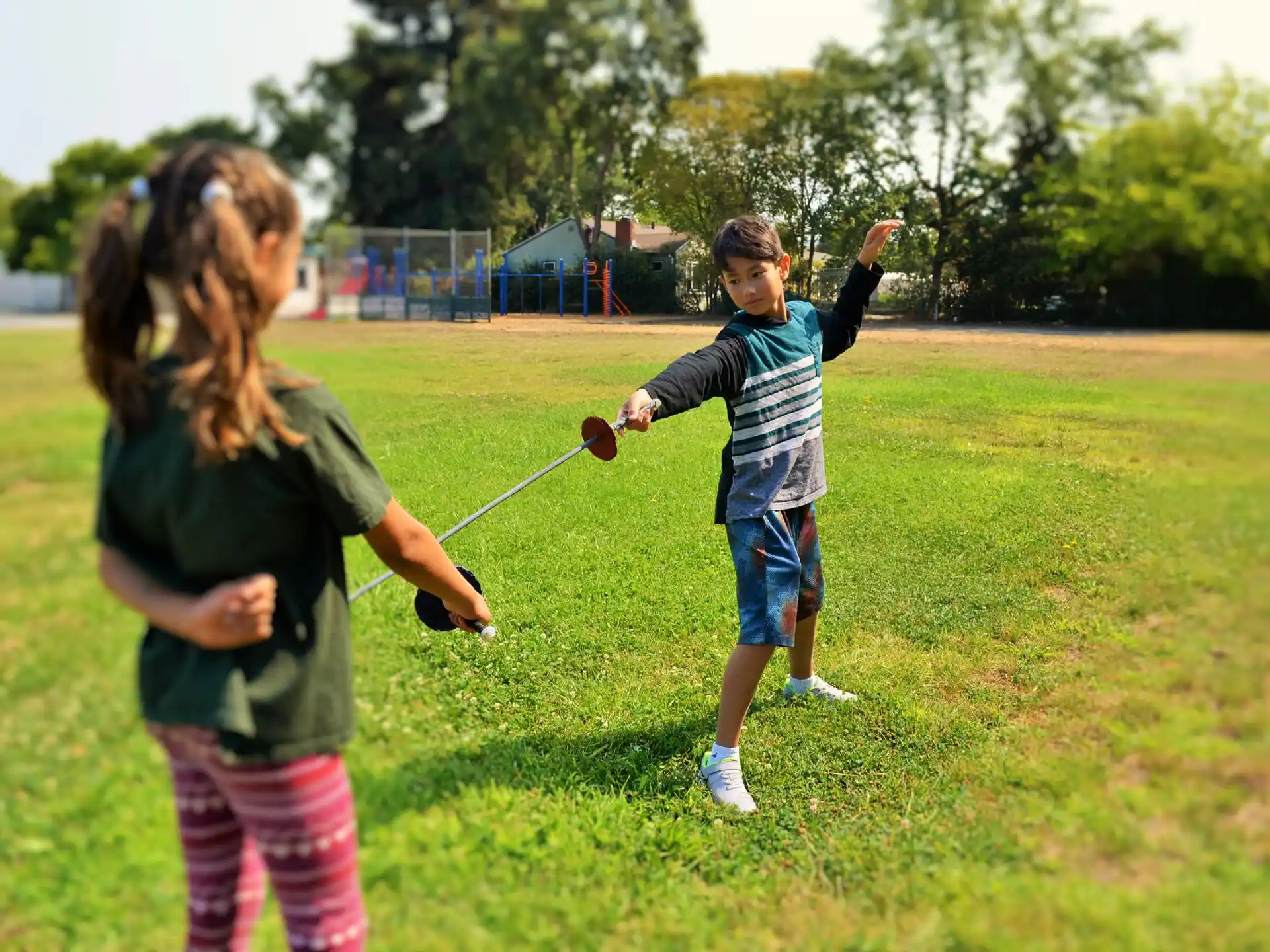 a couple of kids playing with a toy sword in a grassy field