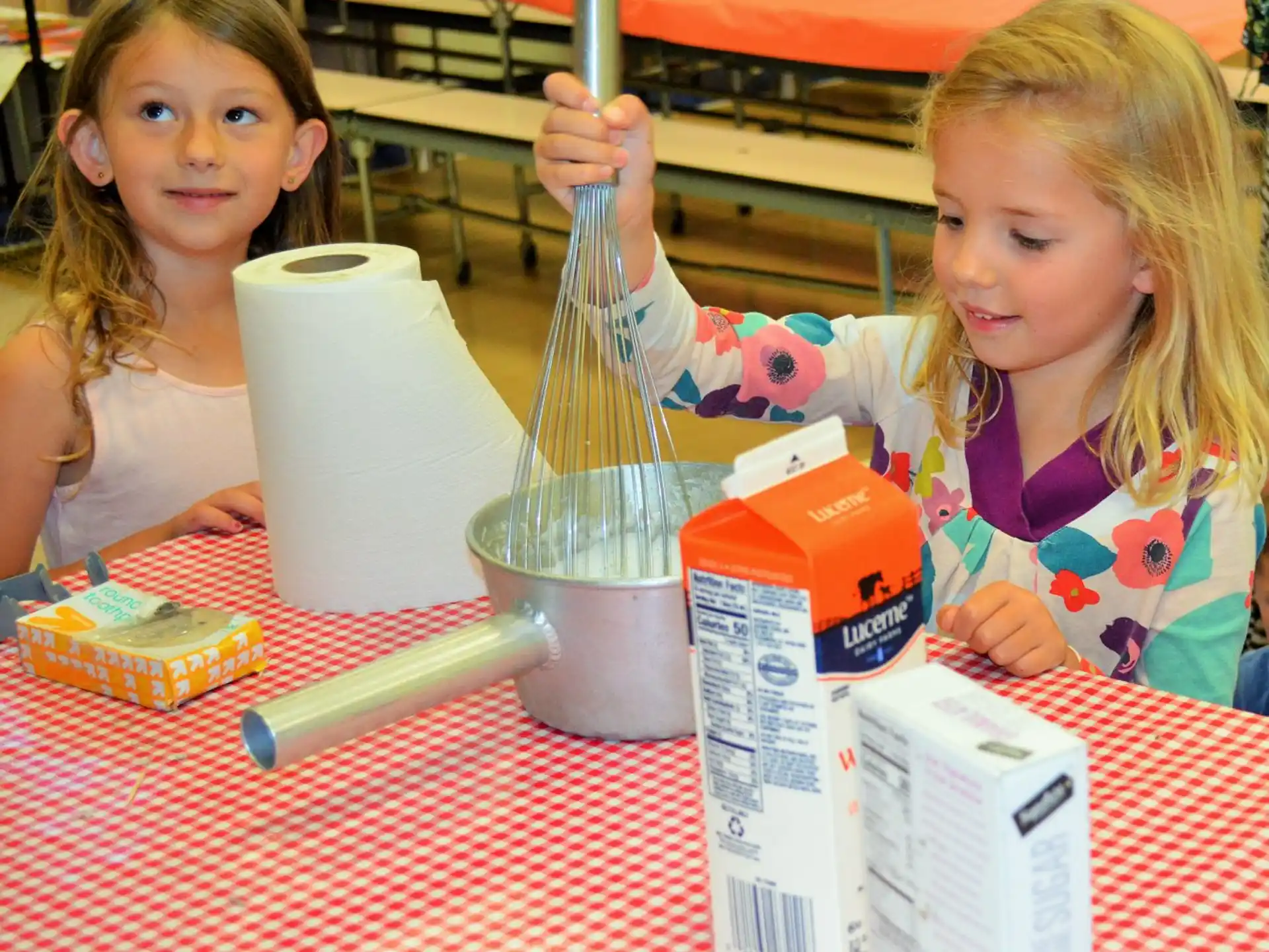 a couple of young girls sitting at a table with a blender and a cup of milk