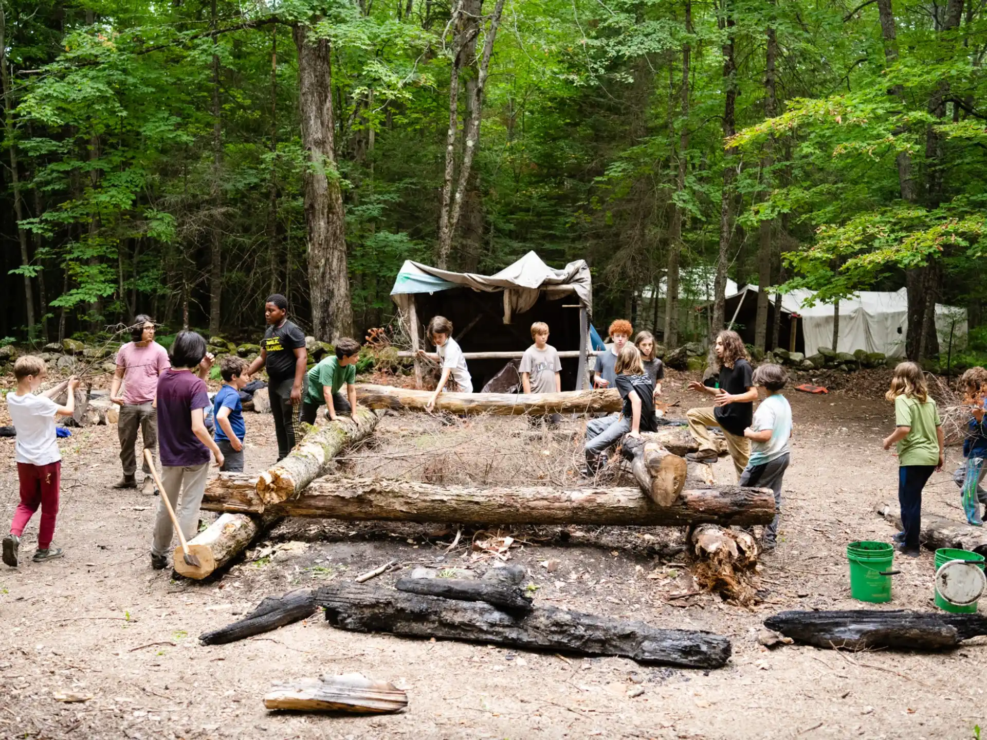 a group of people outside by a log in the woods