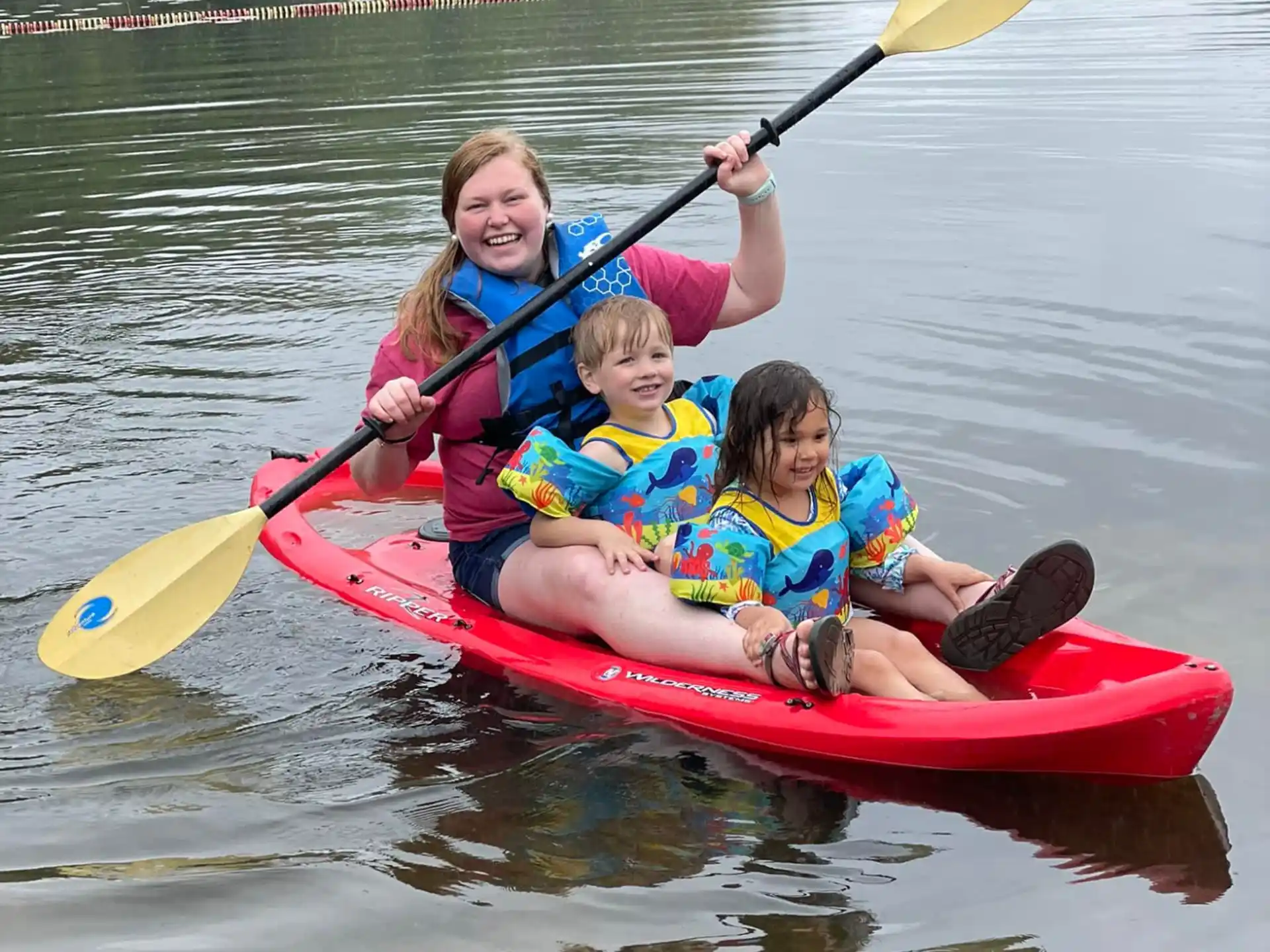 a person and two children in a red kayak on a lake