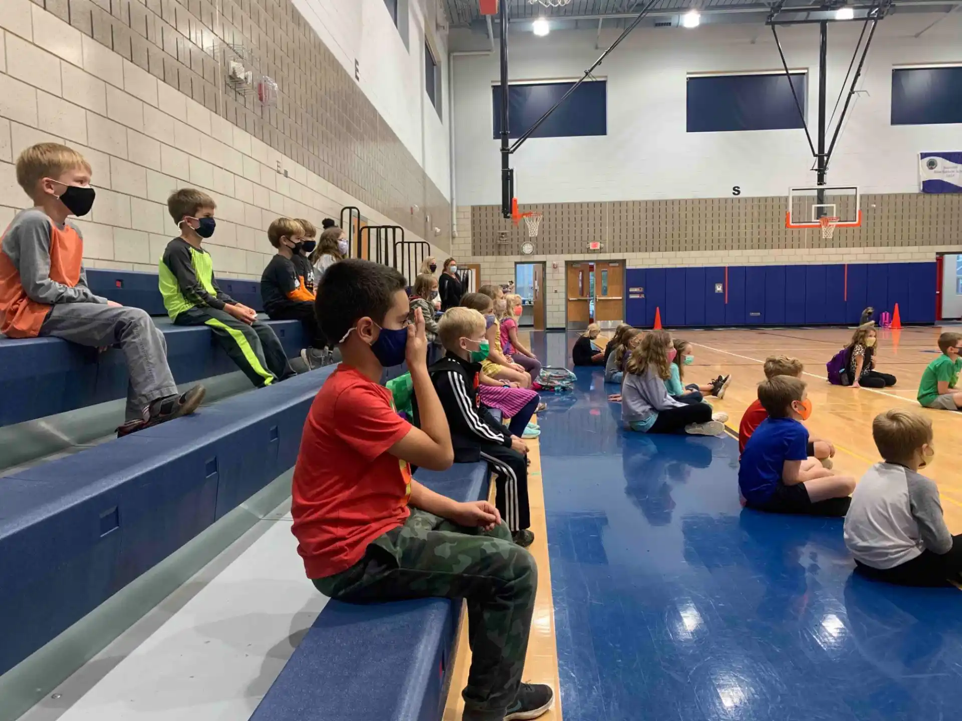 a group of children sitting on a bench in a gymnasium