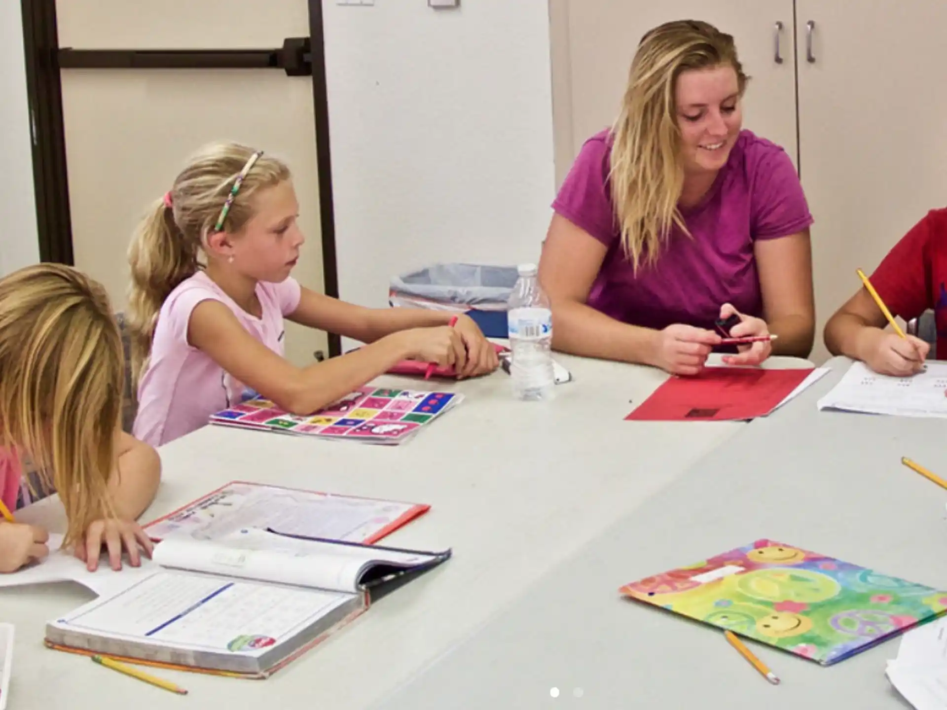 a woman and children sitting at a table with papers and pencils