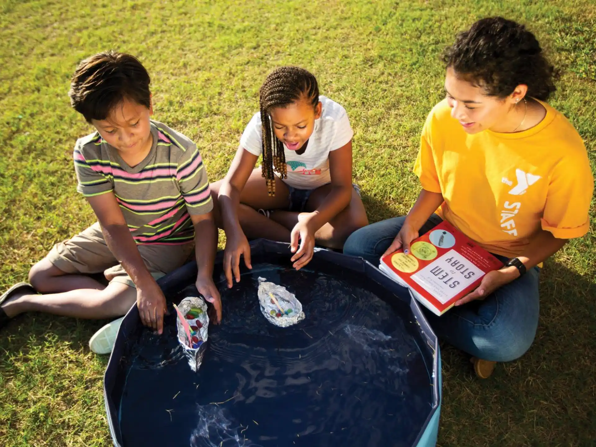 a group of kids sitting on the grass with a blue tent