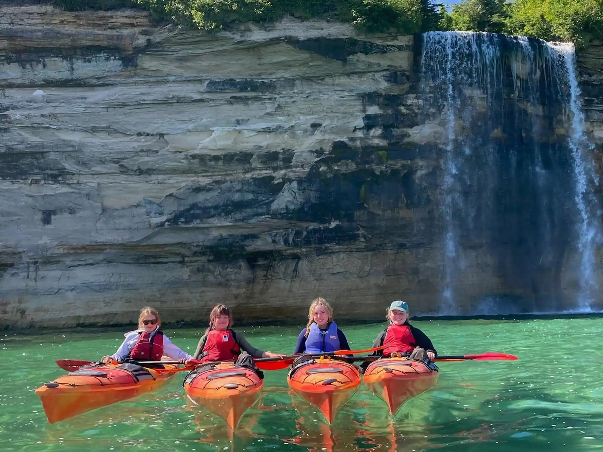 a group of people in kayaks by a waterfall