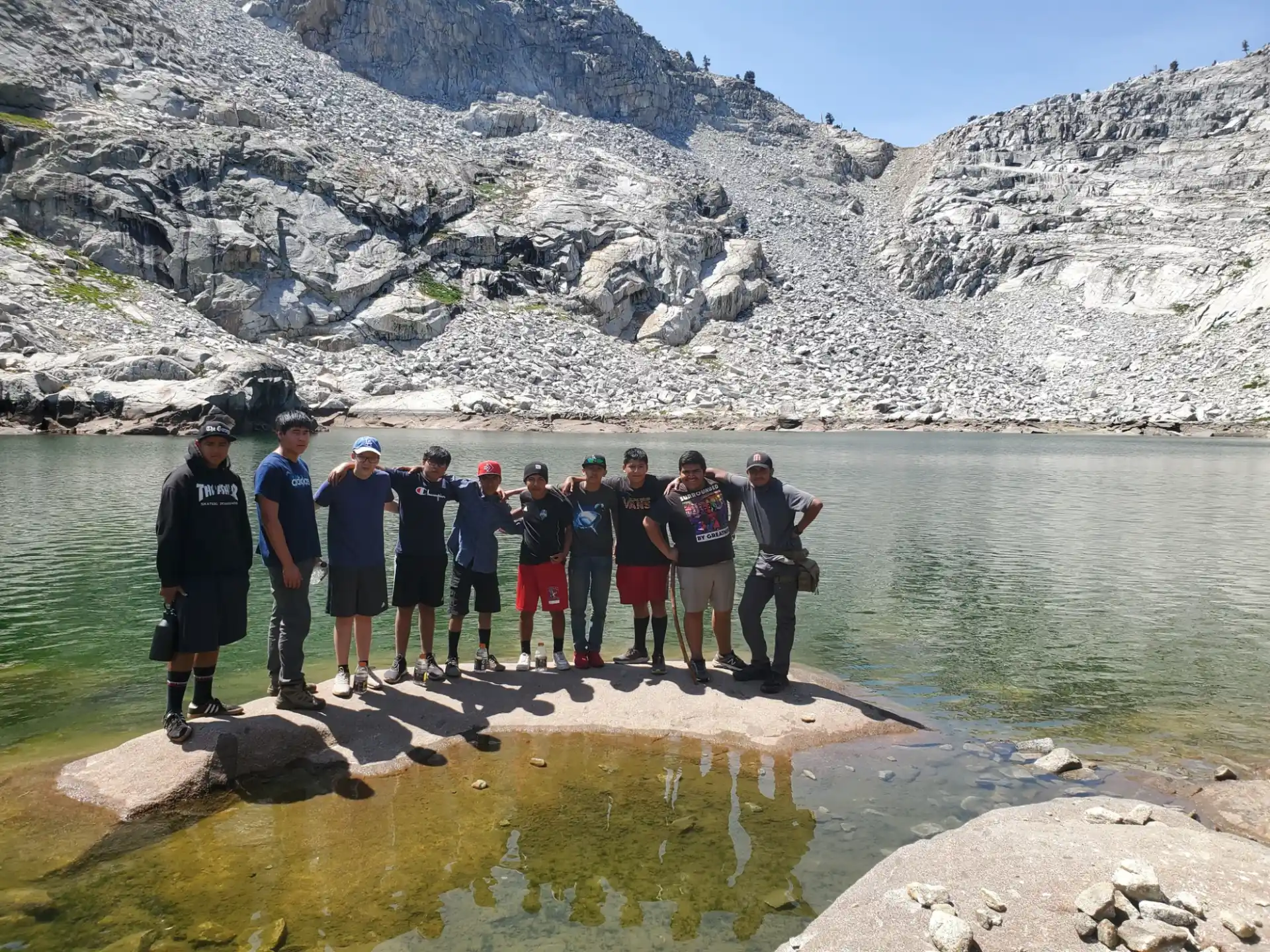 a group of people standing on a rocky shore by a lake