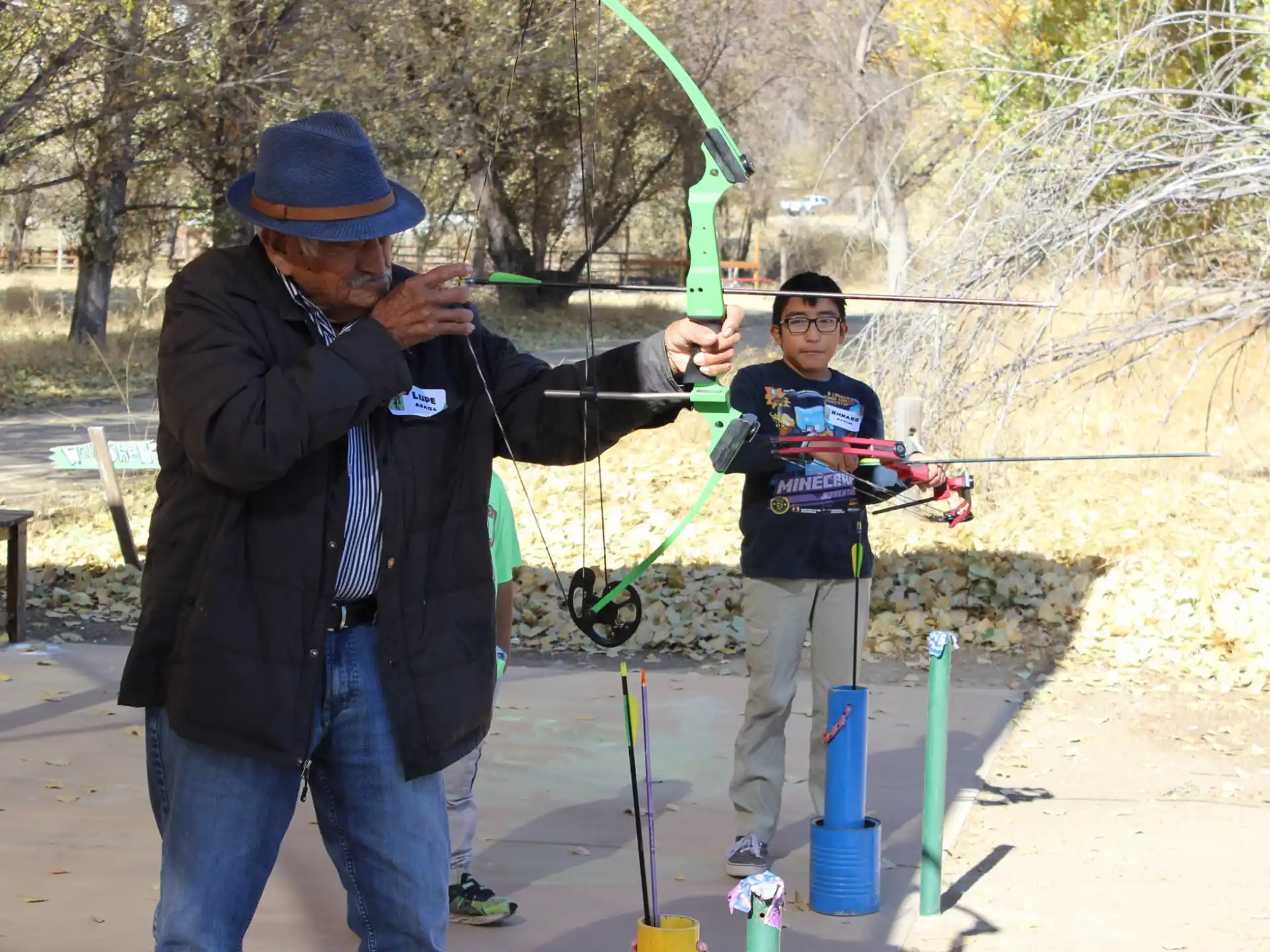 a person holding a bow and arrow next to a boy holding a bow