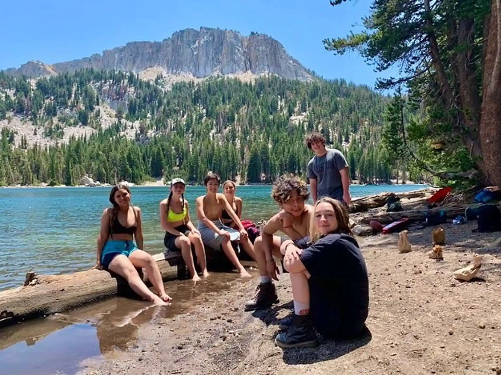 a group of people sitting on a log by a lake