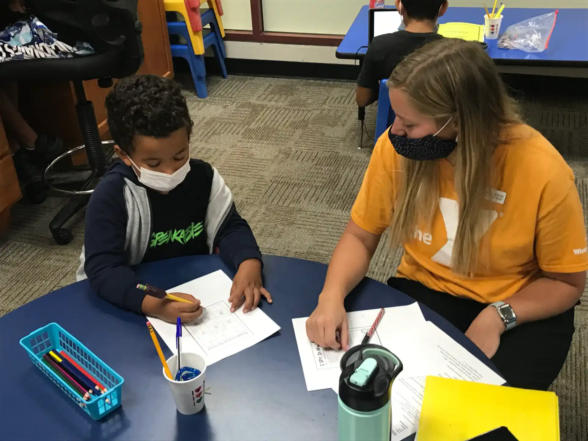 a person and a boy sitting at a table with a paper and pencils