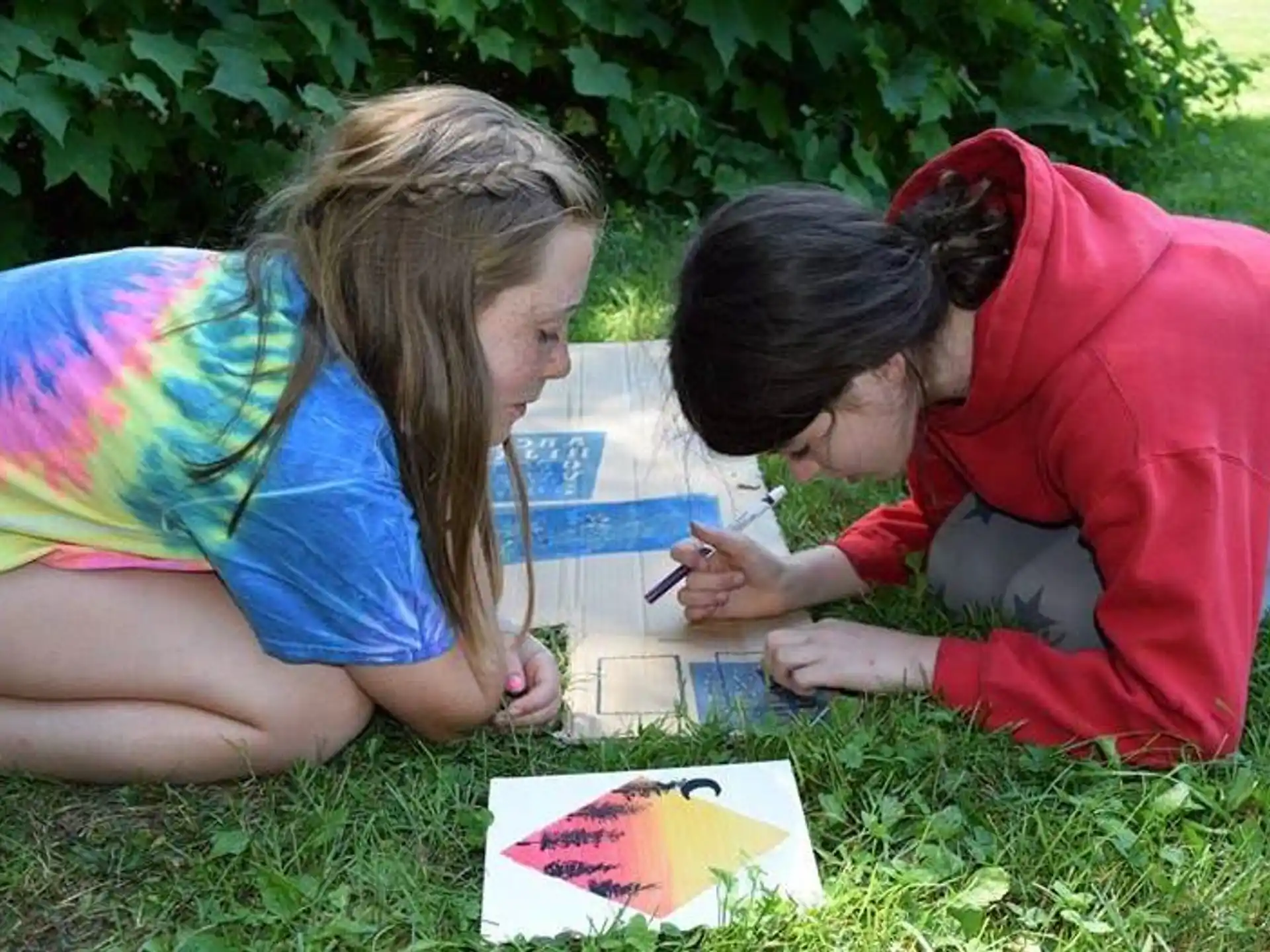 a couple of women sitting on the grass looking at a book