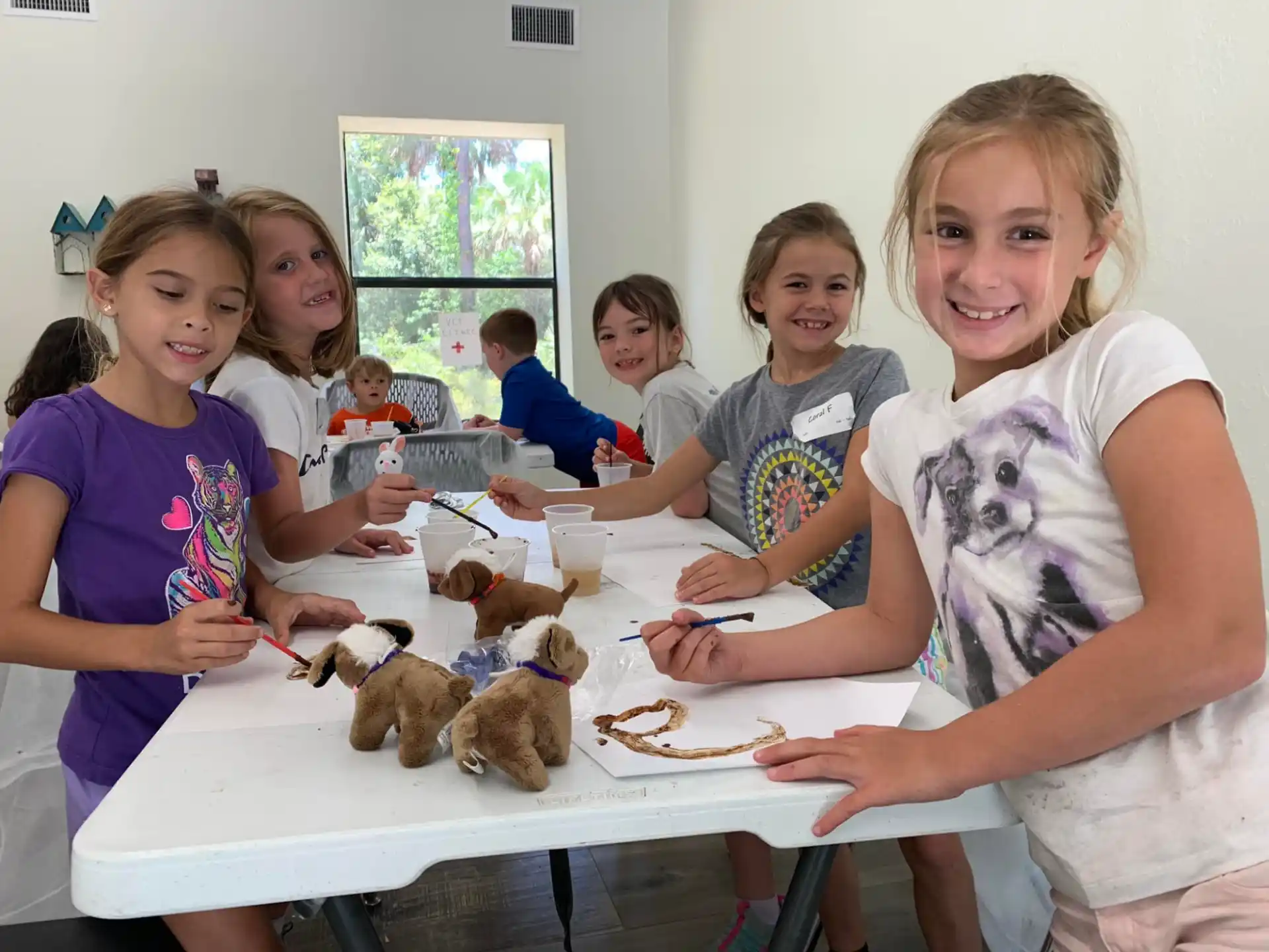 a group of kids sitting around a table with a person holding a plate of cookies
