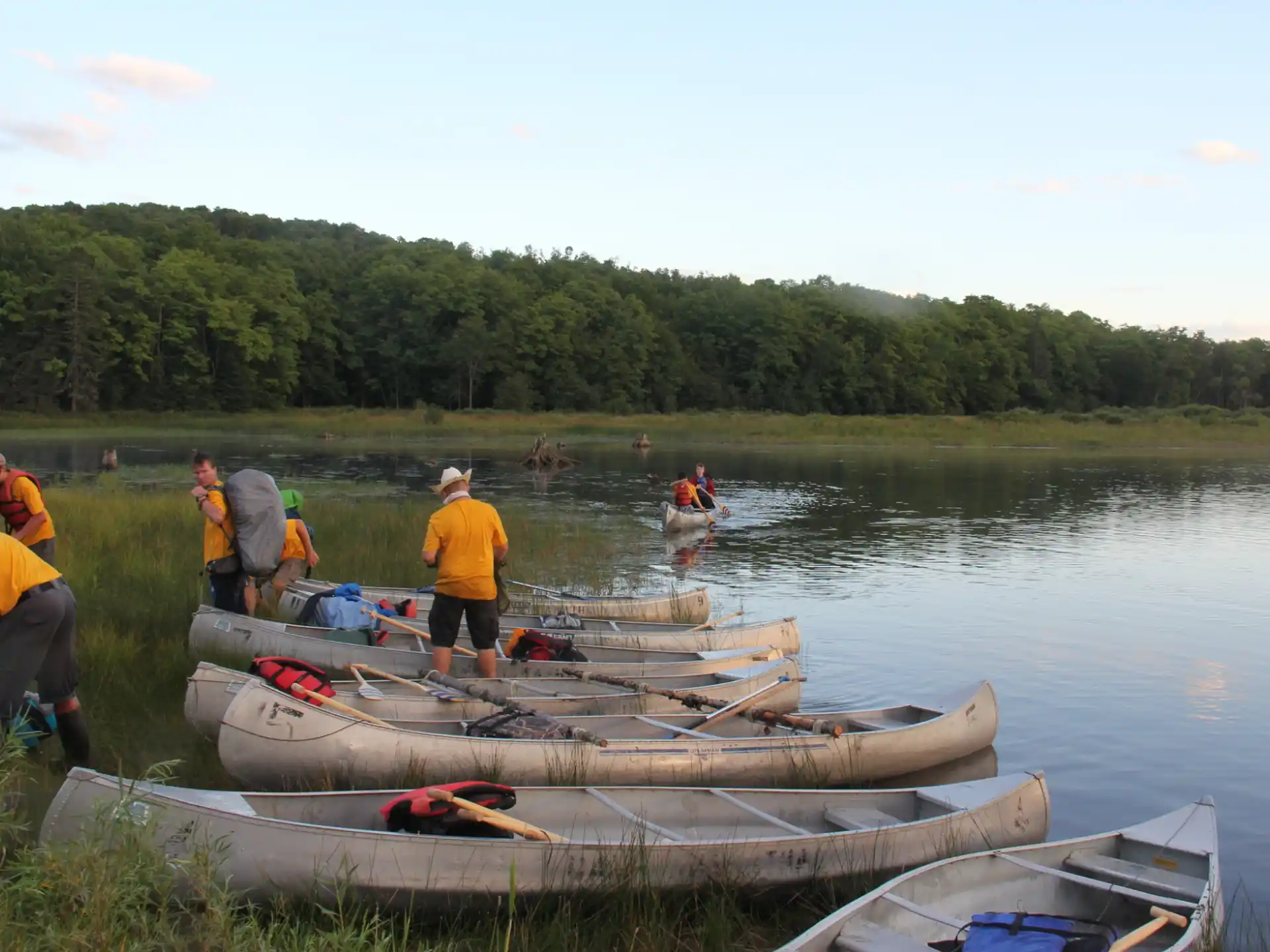 a group of people standing next to a row of canoes on a lake