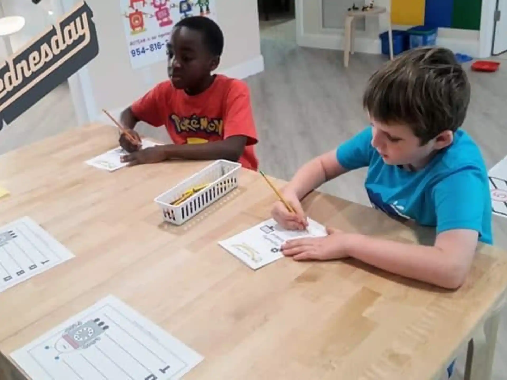 a few young boys sitting at a table with pencils and paper