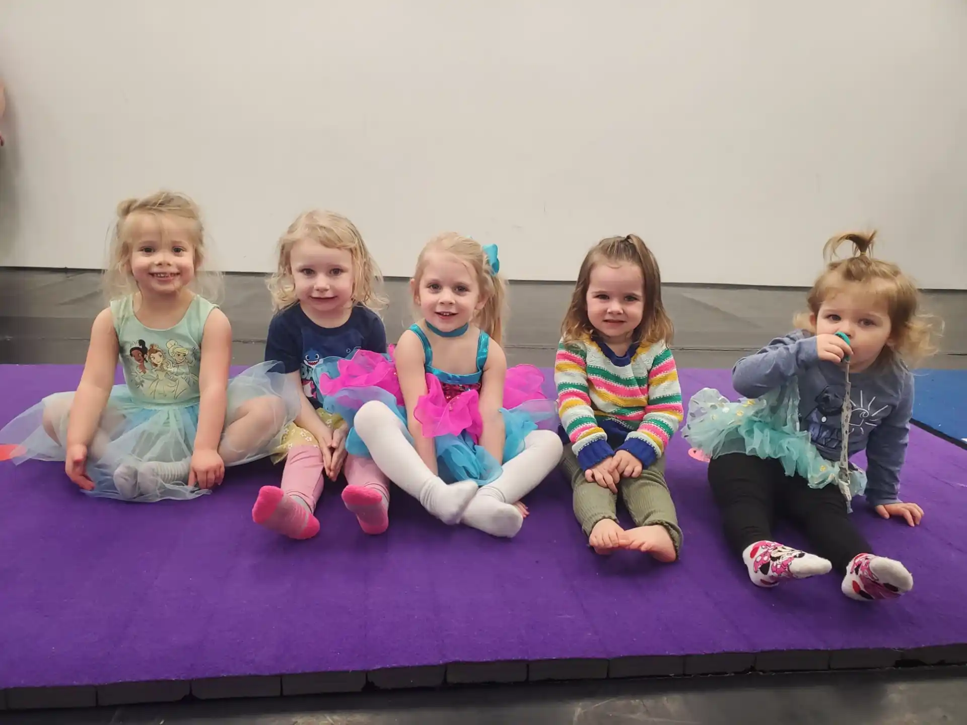 a group of children sitting on a mat with toothbrushes in their mouths